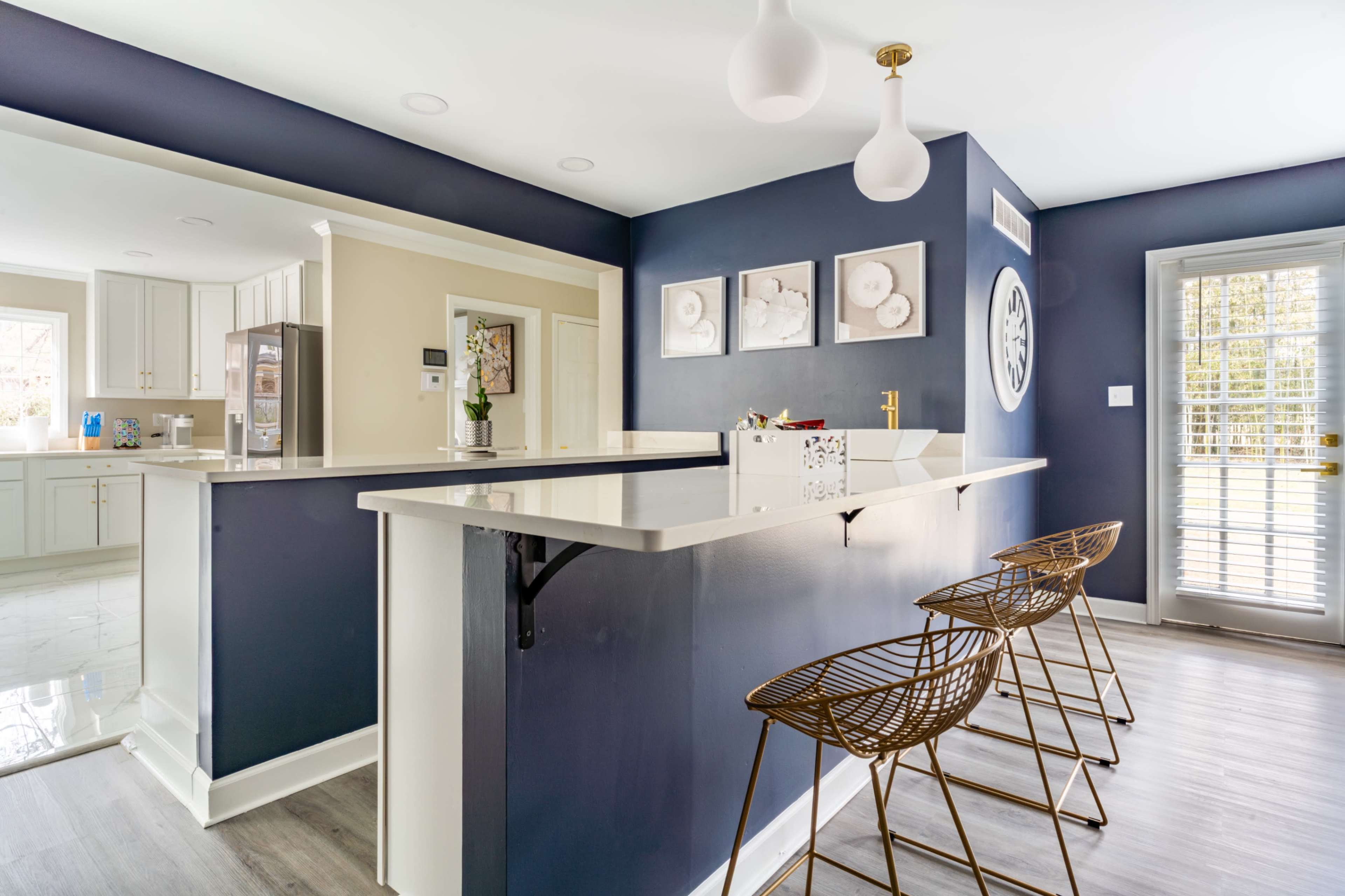 The image shows a modern kitchen featuring a blue accent wall, a white countertop with bar seating, and a doorway leading to another room.