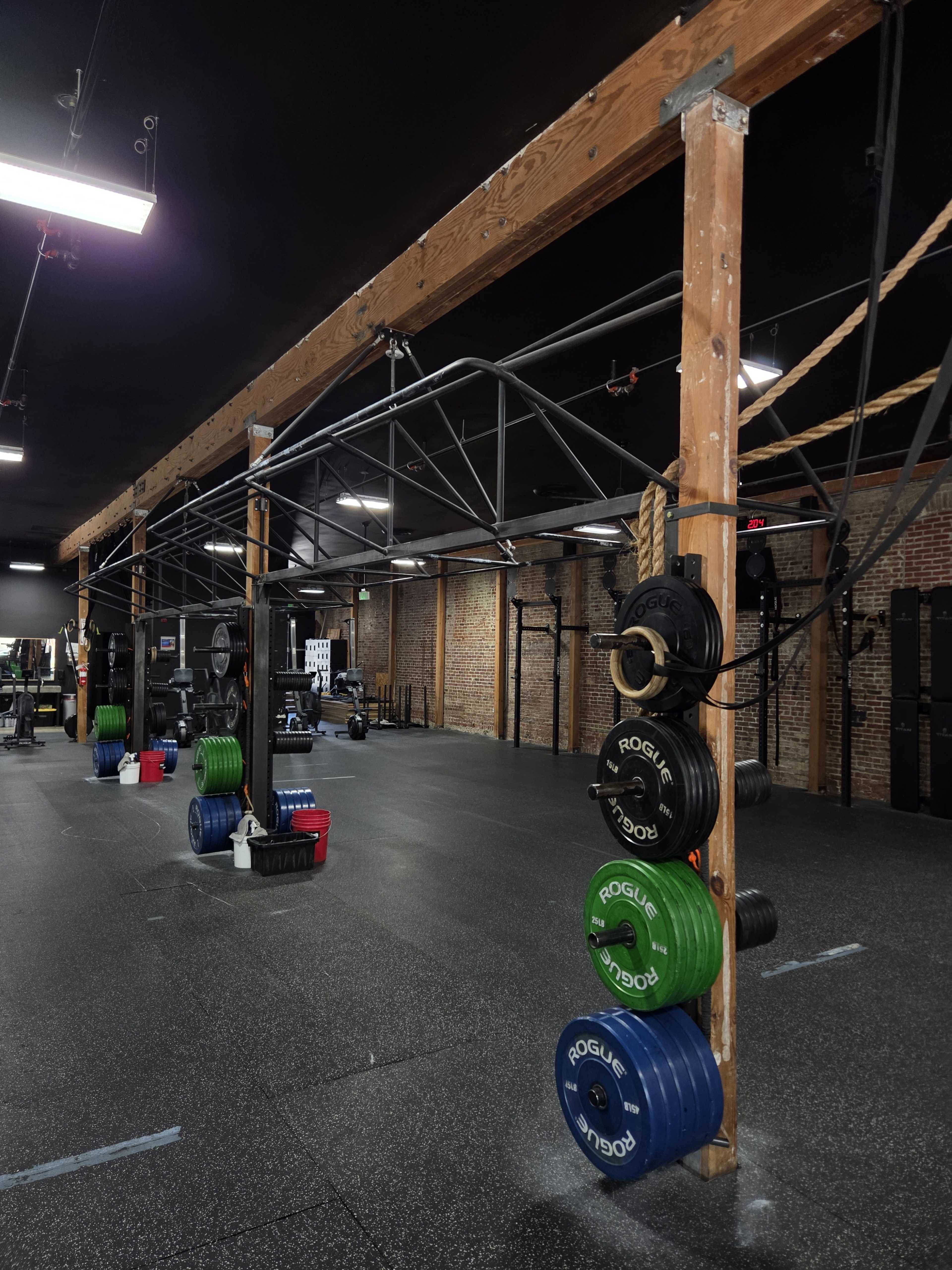 The image shows a spacious gym with weightlifting equipment and fitness accessories arranged neatly, featuring a rack of colorful weight plates on one side.