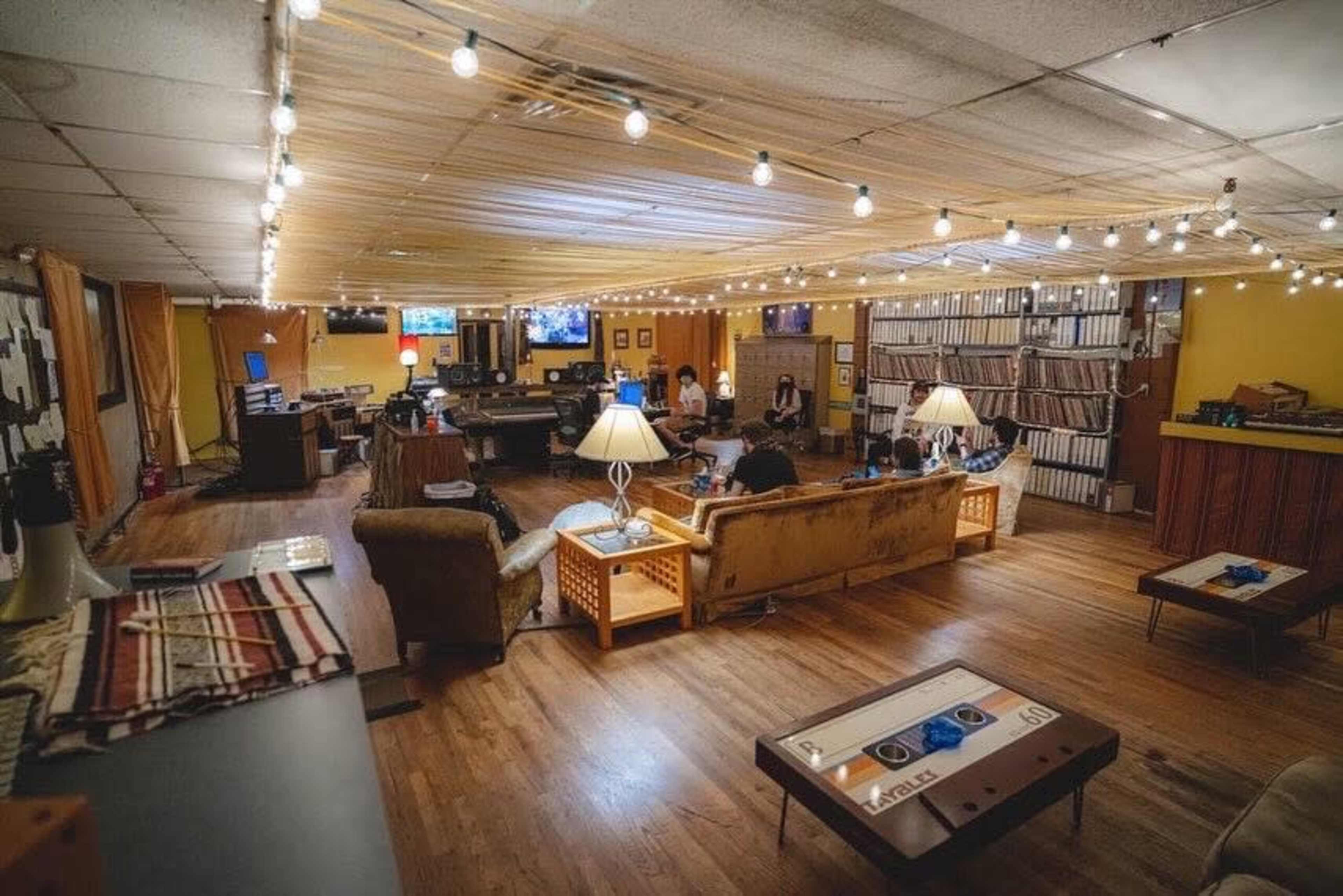 The image shows a spacious, well-lit lounge area with several couches, tables, and screens, where people are seated and engaging in various activities.