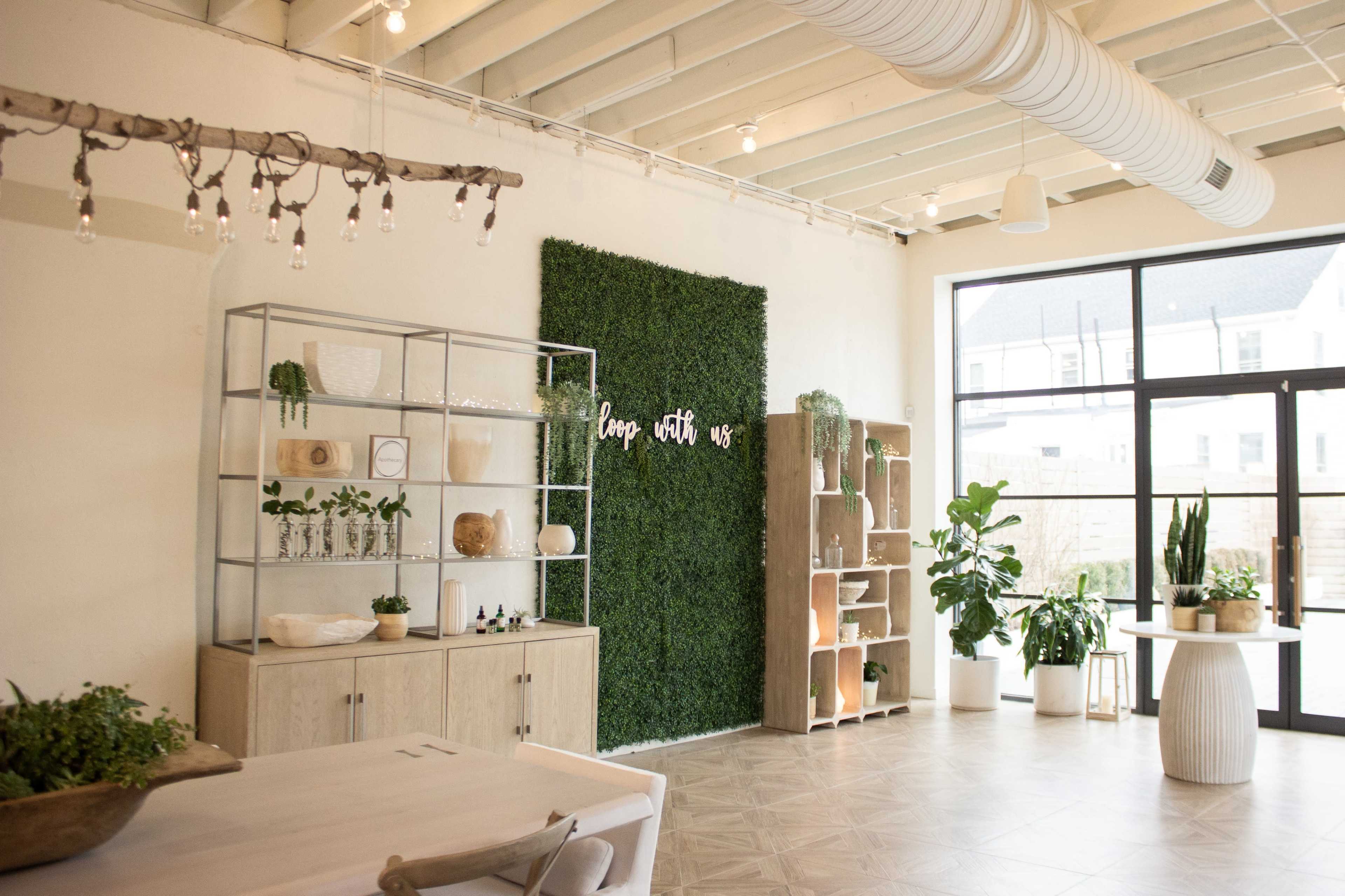 The image shows a bright, modern interior featuring green plants, shelving units, and a decorative wall with the phrase "happy with us."