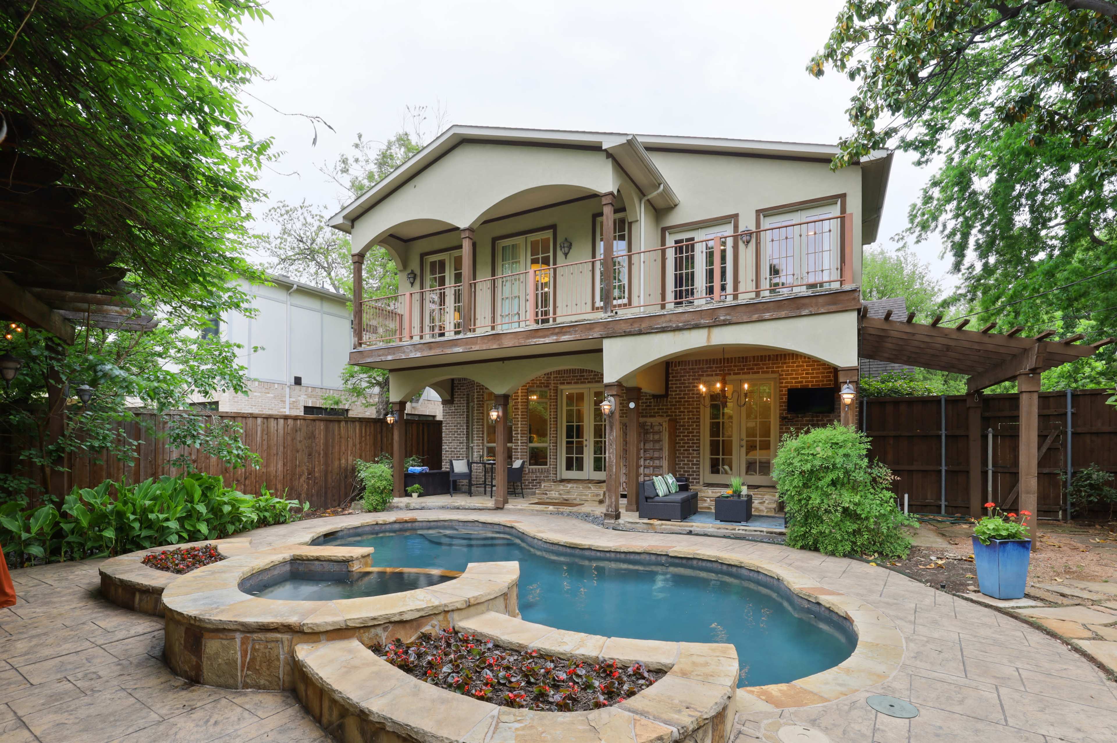The image shows a two-story house with a backyard that features a curved swimming pool, stone patio, and a small garden area.