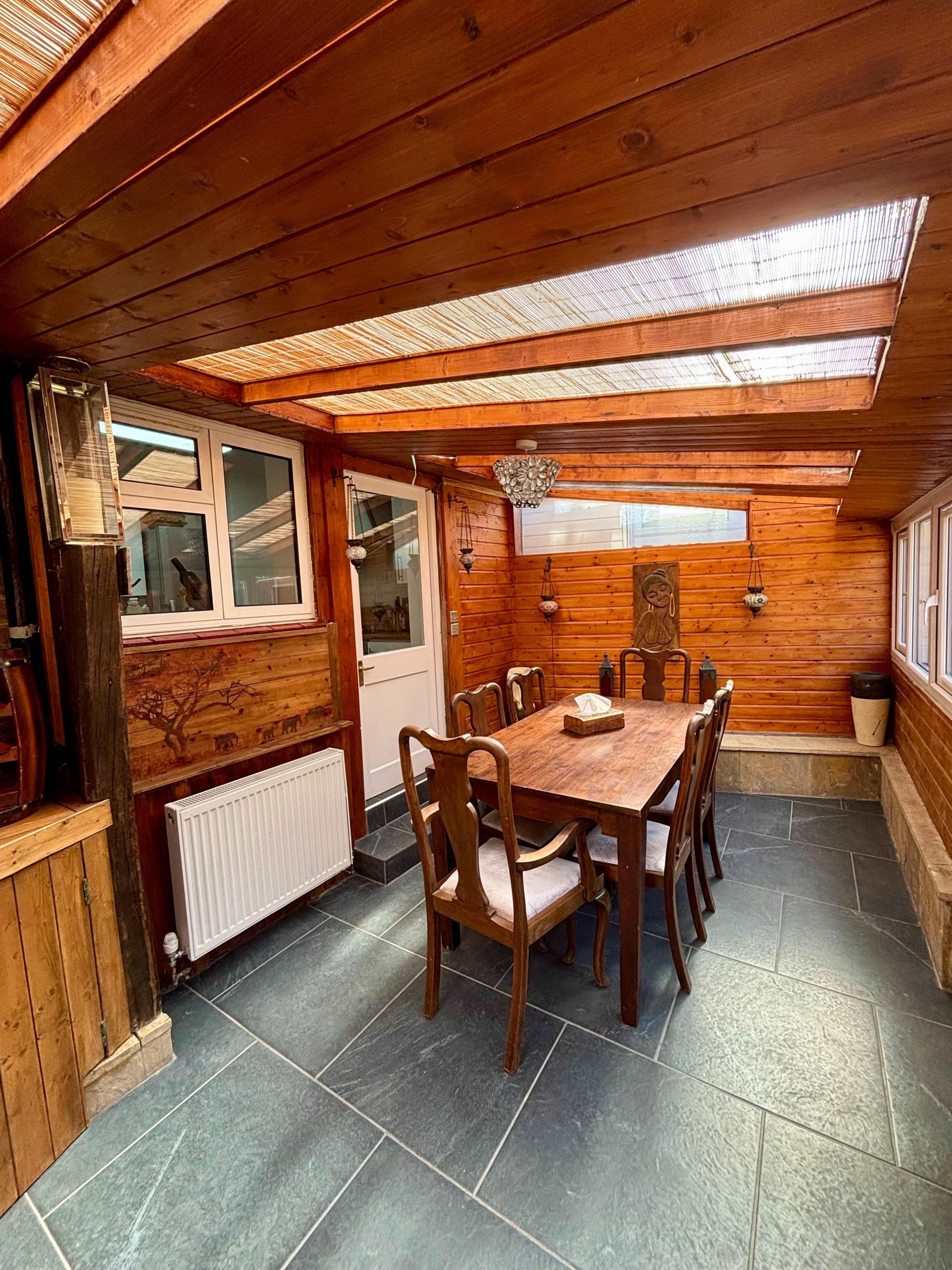 The image shows a wooden dining area with a large table and chairs, illuminated by natural light through skylights above.