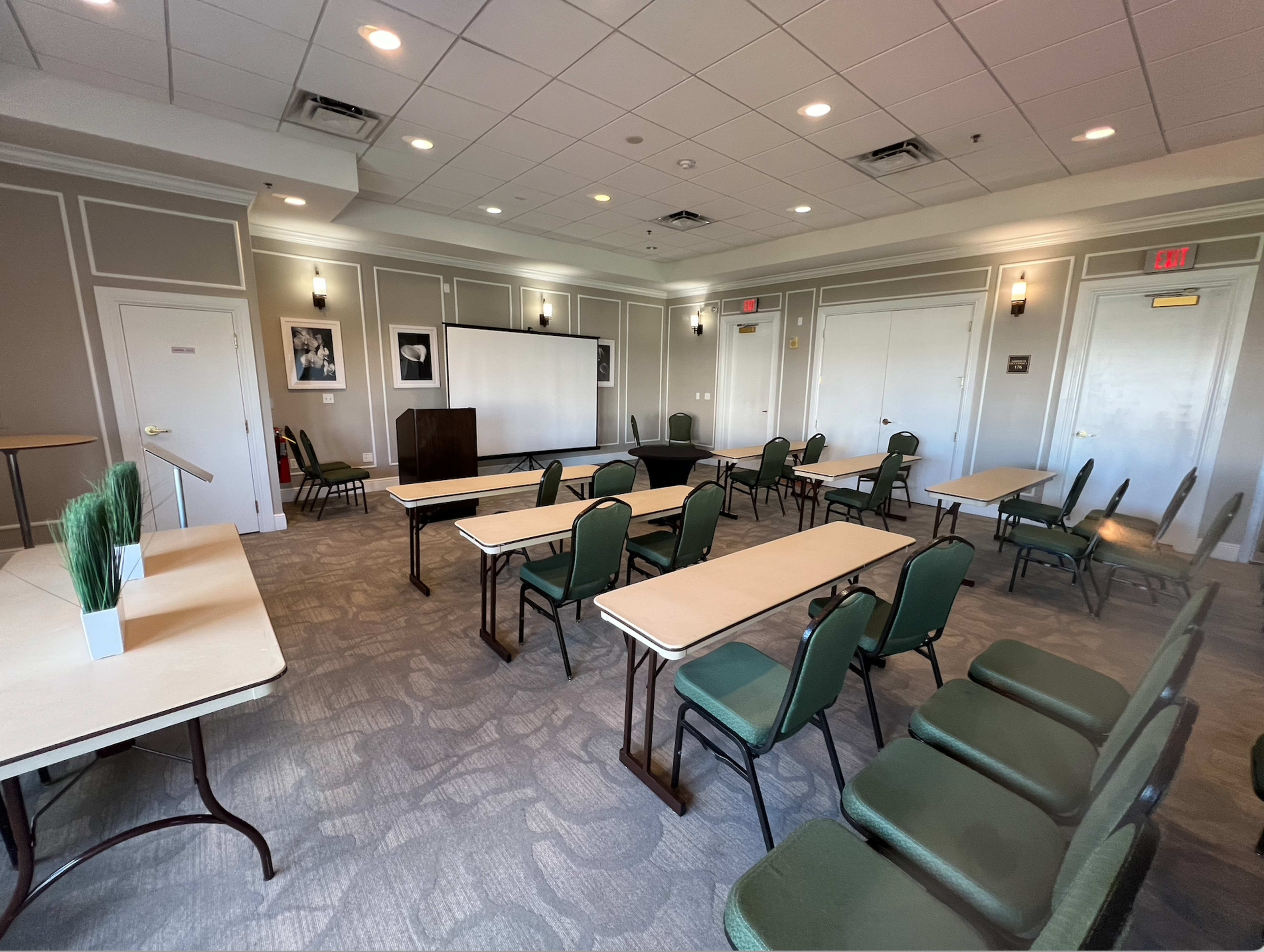 The image shows a meeting room with multiple tables arranged in rows and green chairs positioned around them.
