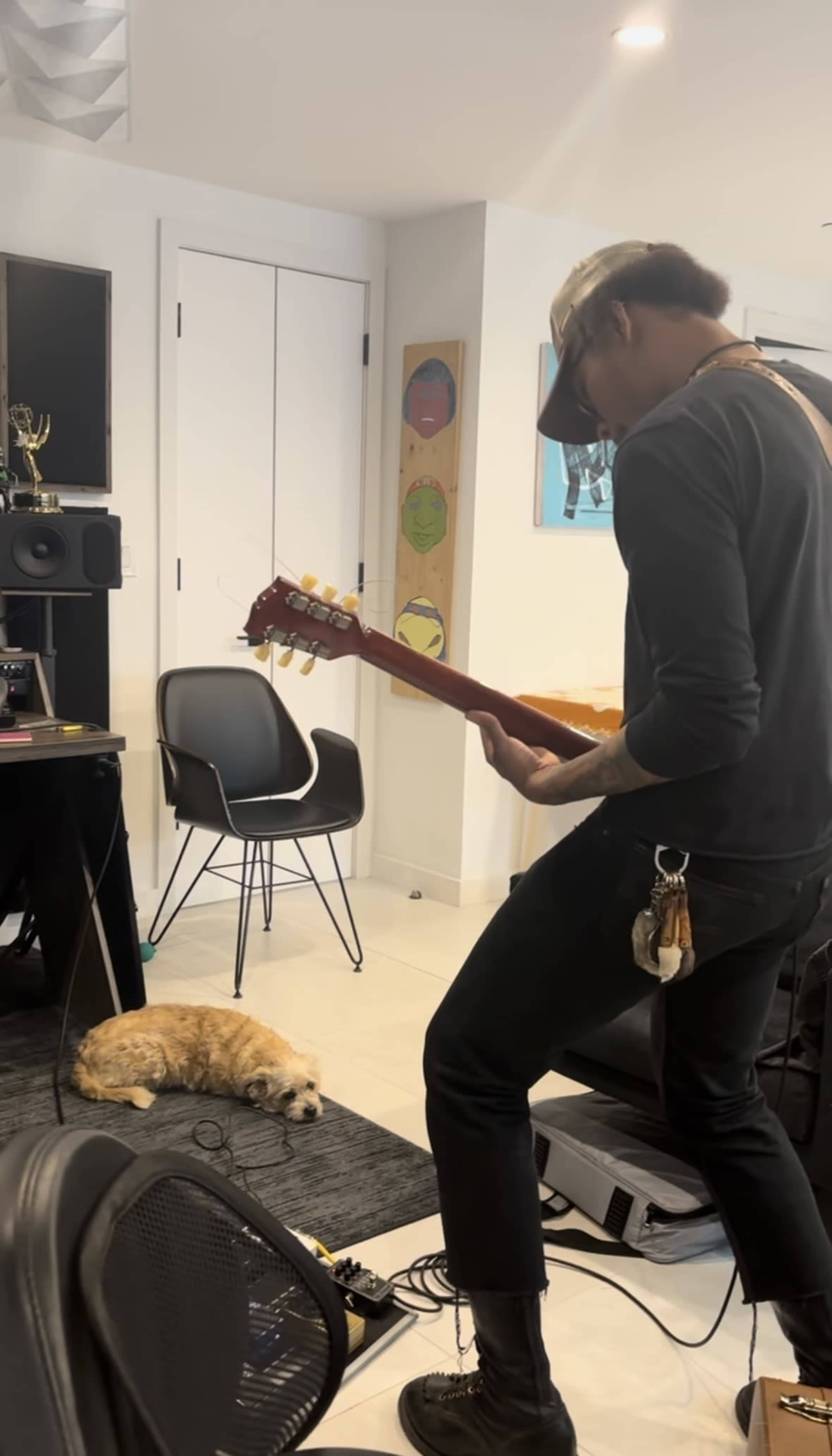 A person plays guitar in a music studio while a dog lies on the floor nearby.