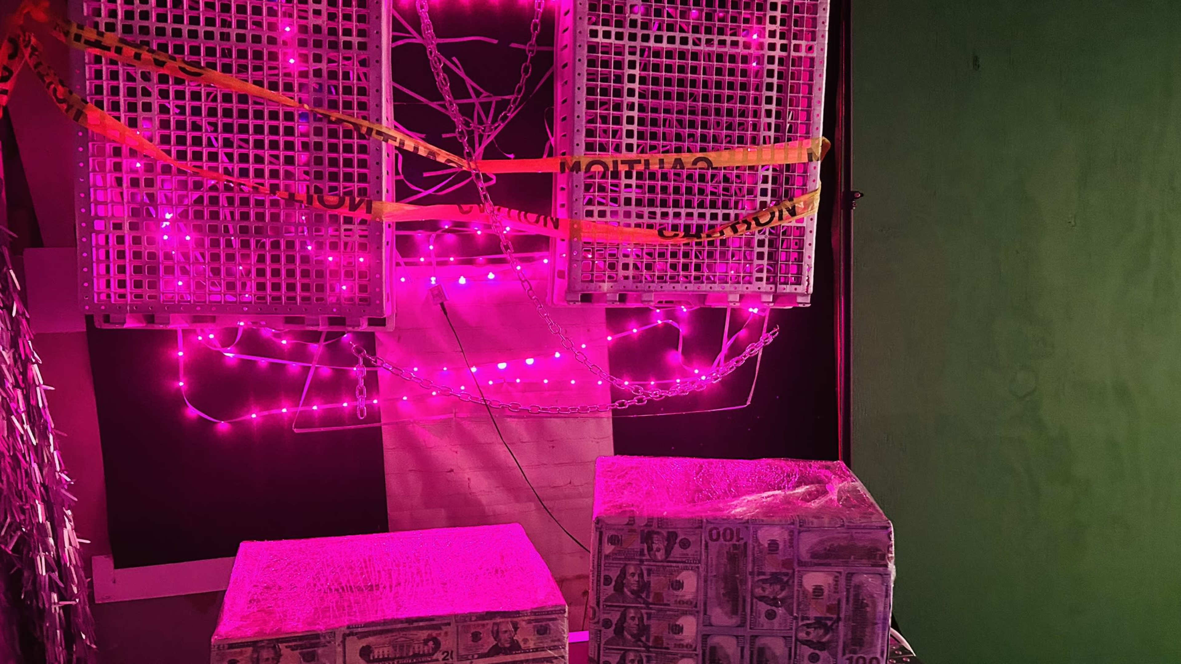 A wall adorned with pink lights and two elevated structures, each covered with a grid pattern and secured with caution tape.