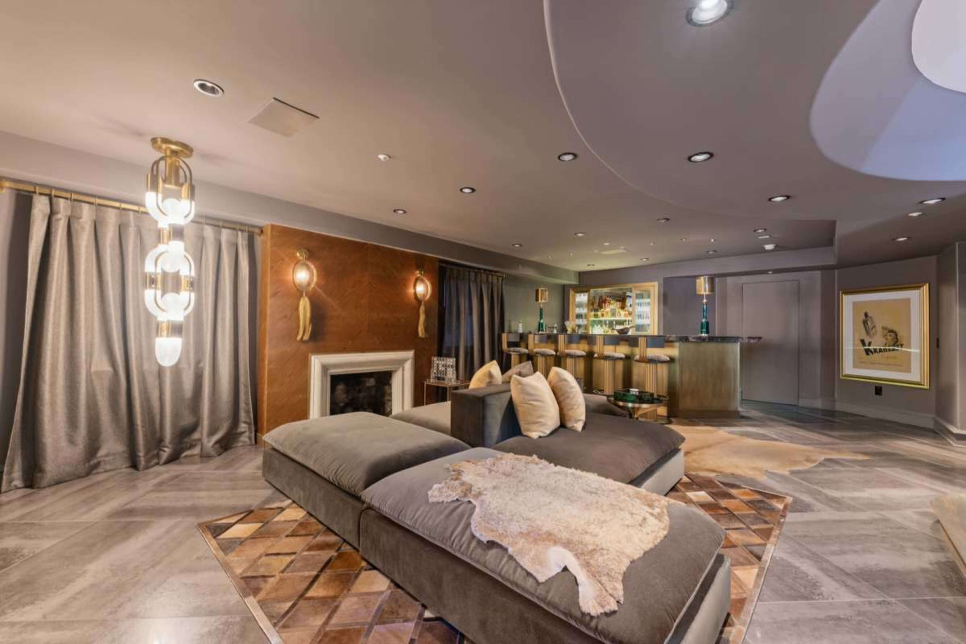 The image depicts a modern living space featuring a sectional sofa, a bar area, and a fireplace, complemented by gray curtains and decorative accents.