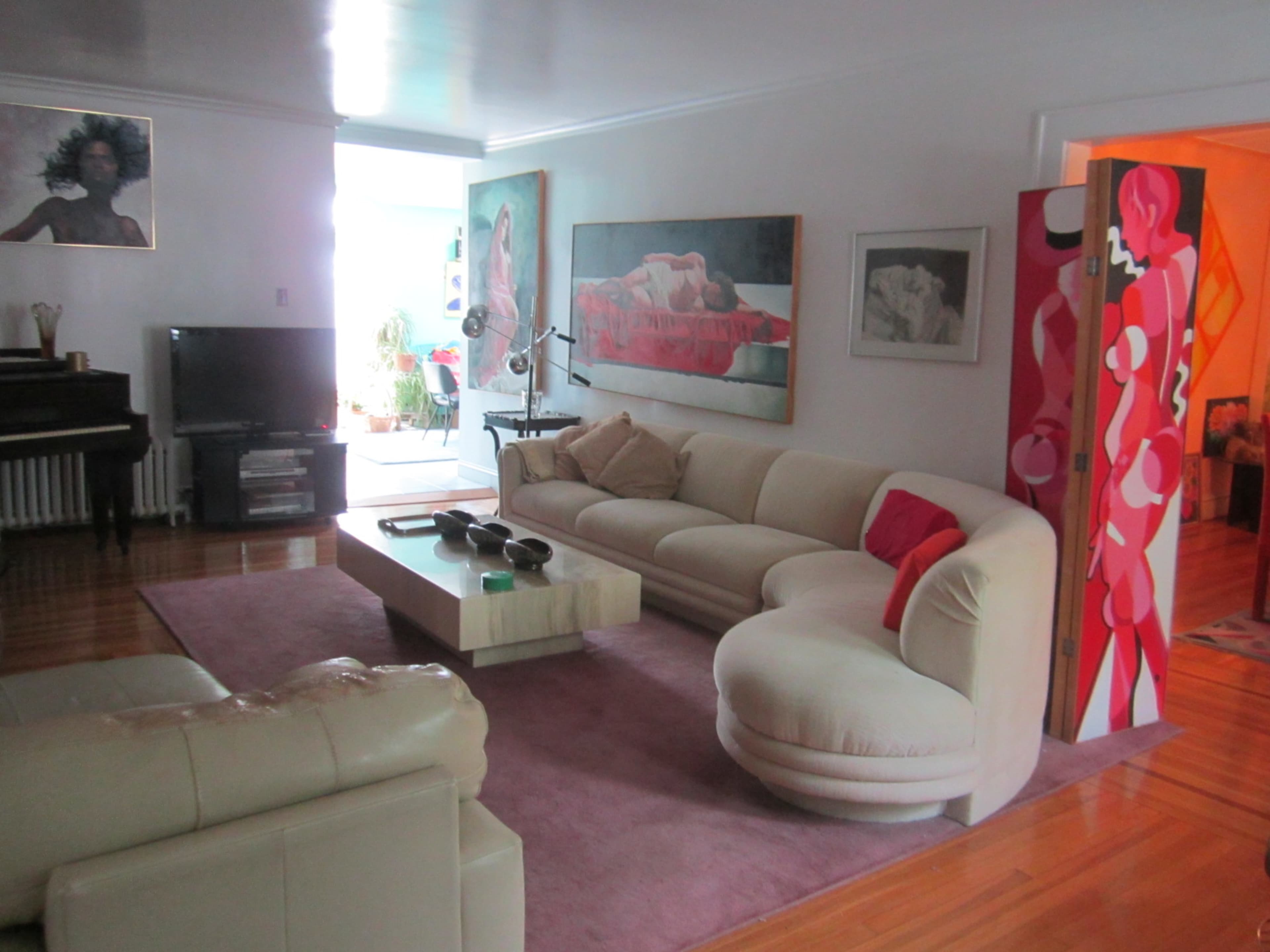 A living room with a curved white sofa, a wooden coffee table, and several pieces of artwork on the walls.