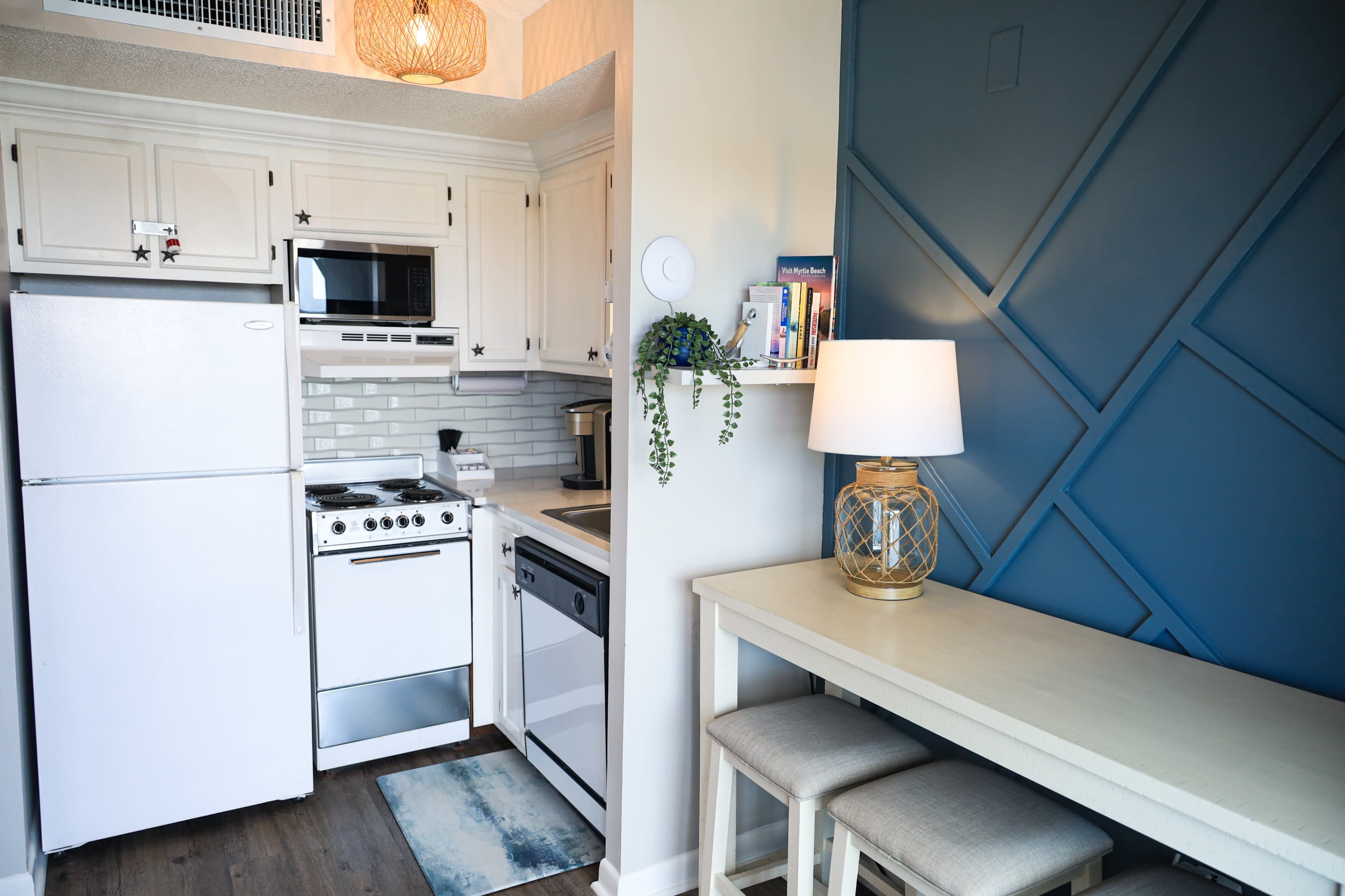 A compact kitchen area with white cabinets, a stove, and a small dining table with stools against a blue accent wall.