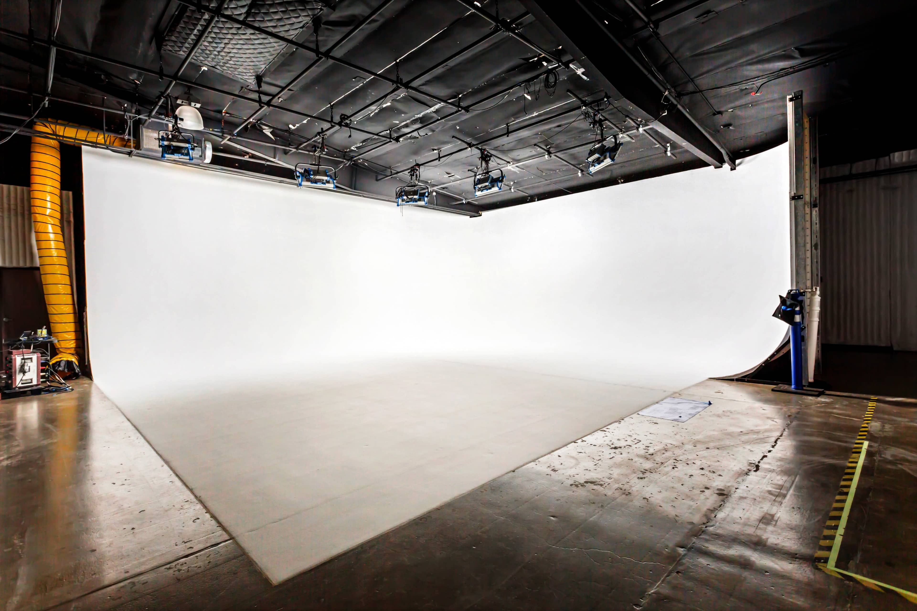 The image shows a spacious, empty photography studio with a large white backdrop and overhead lighting.