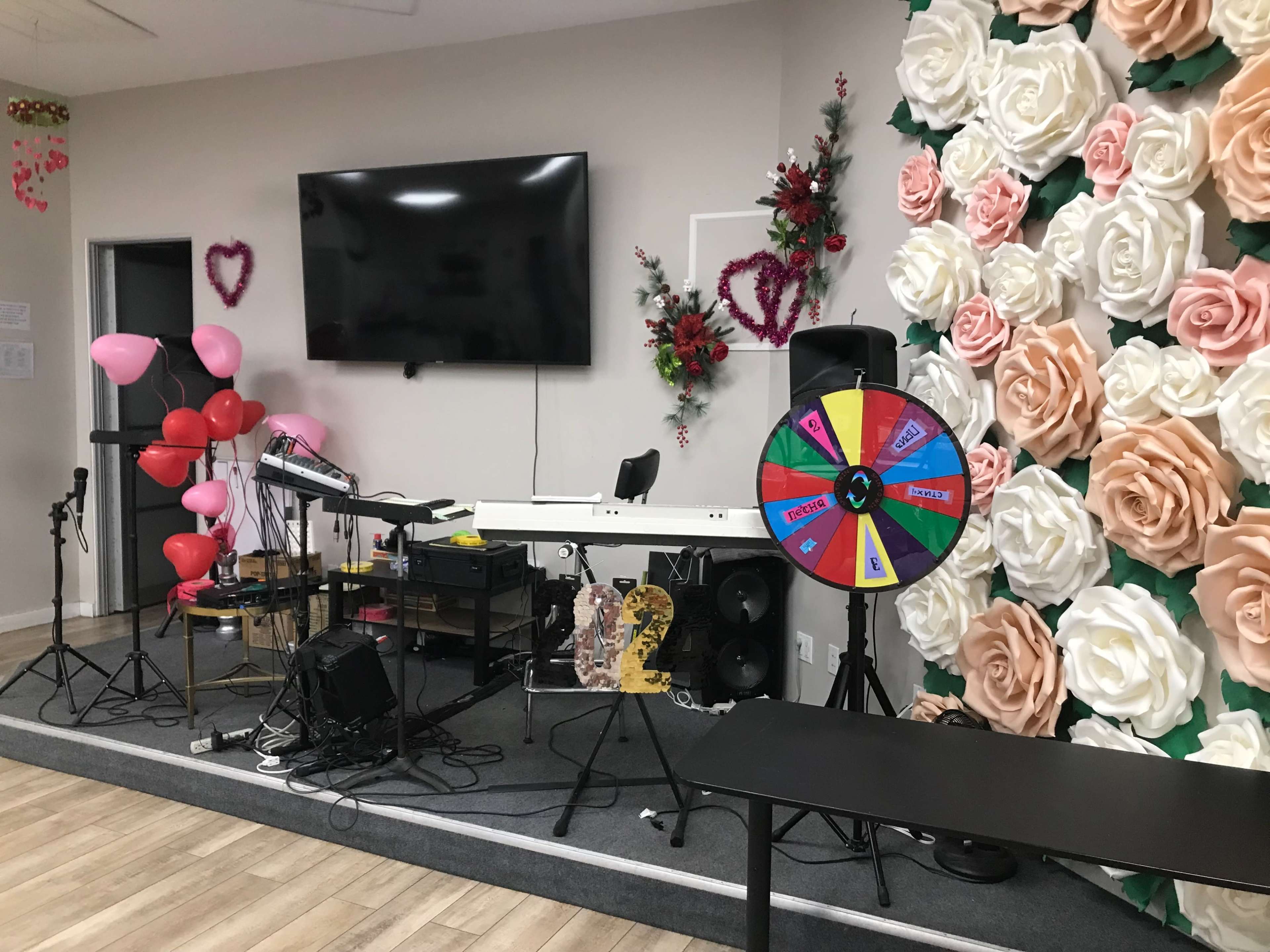 A decorated stage with a keyboard, a spinning wheel, balloons, and a floral backdrop made of large paper flowers.