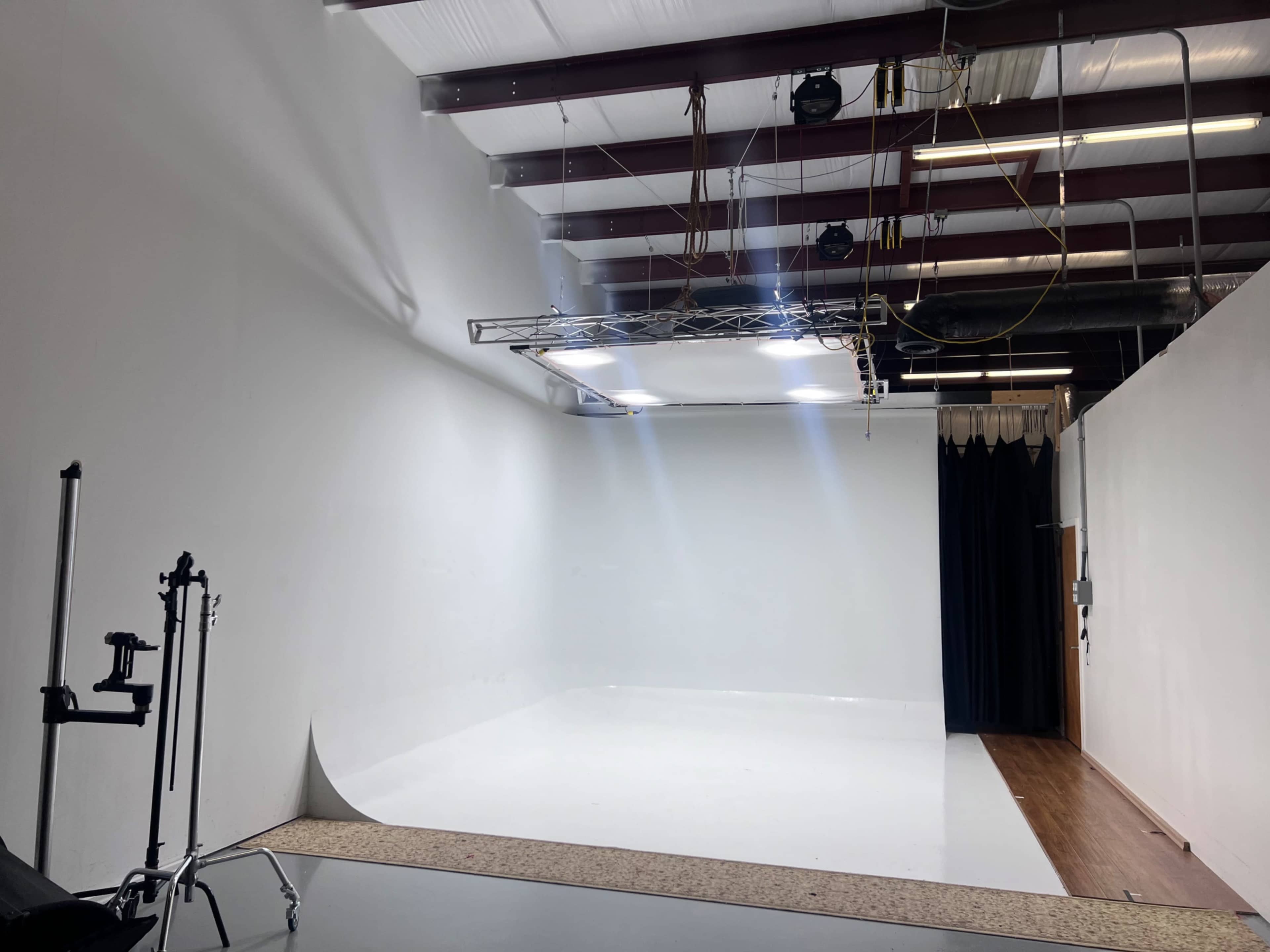 A spacious studio with white walls, a seamless backdrop, and overhead lighting equipment.