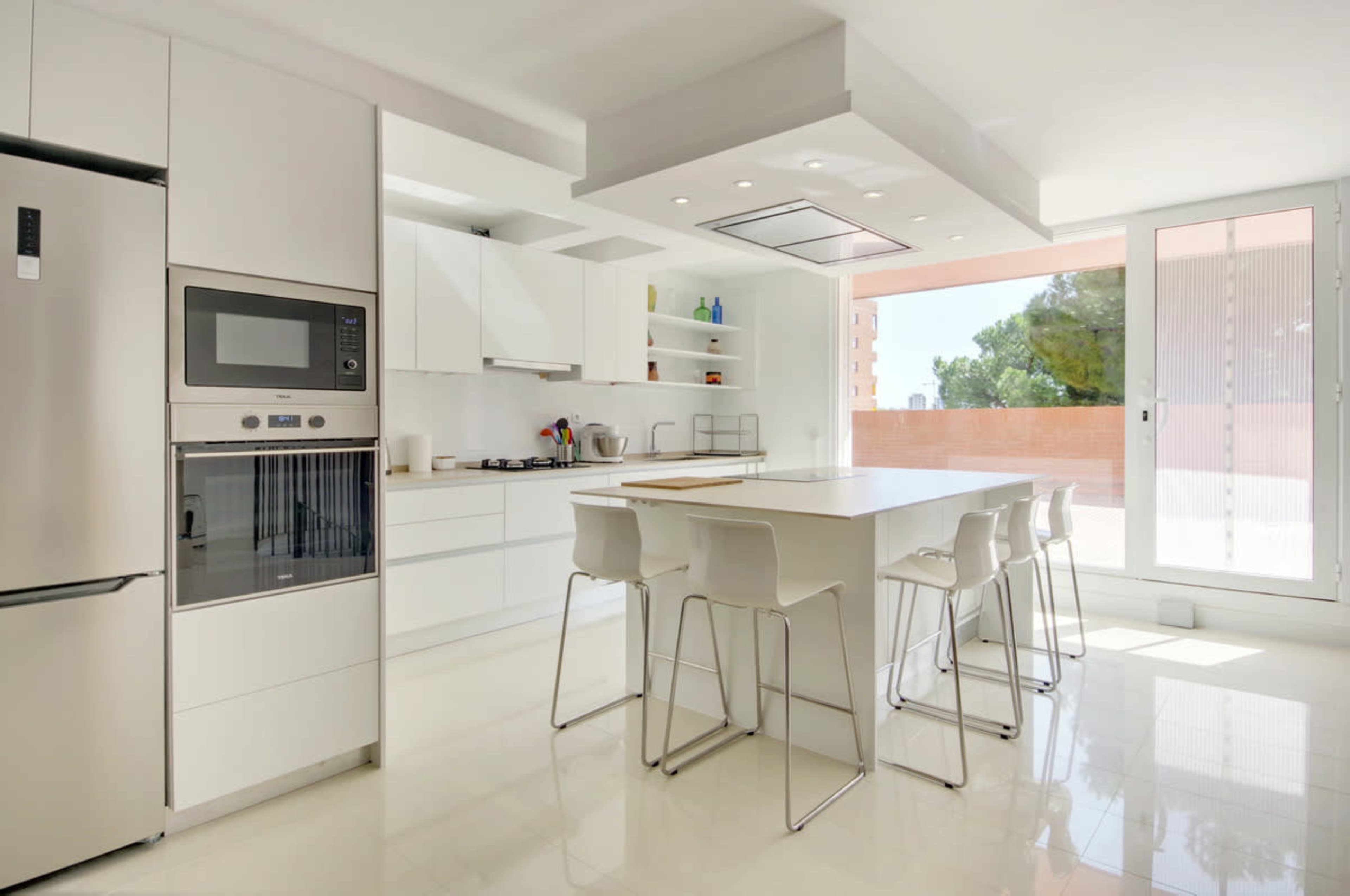 A modern kitchen features sleek white cabinetry, stainless steel appliances, and a large central island with seating.