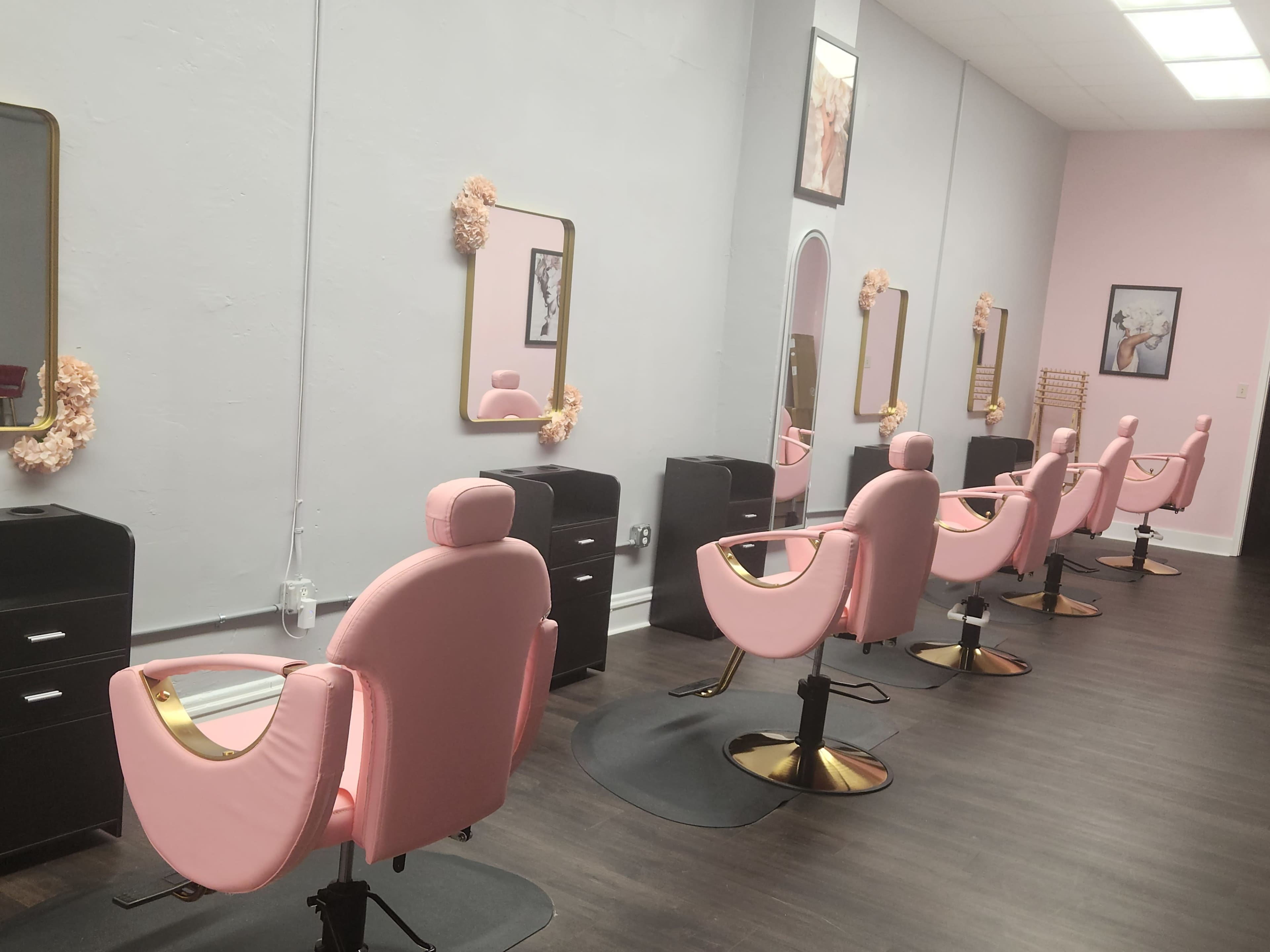 The image shows a beauty salon interior with six pink salon chairs facing mirrors, black storage units nearby, and a light gray wall.