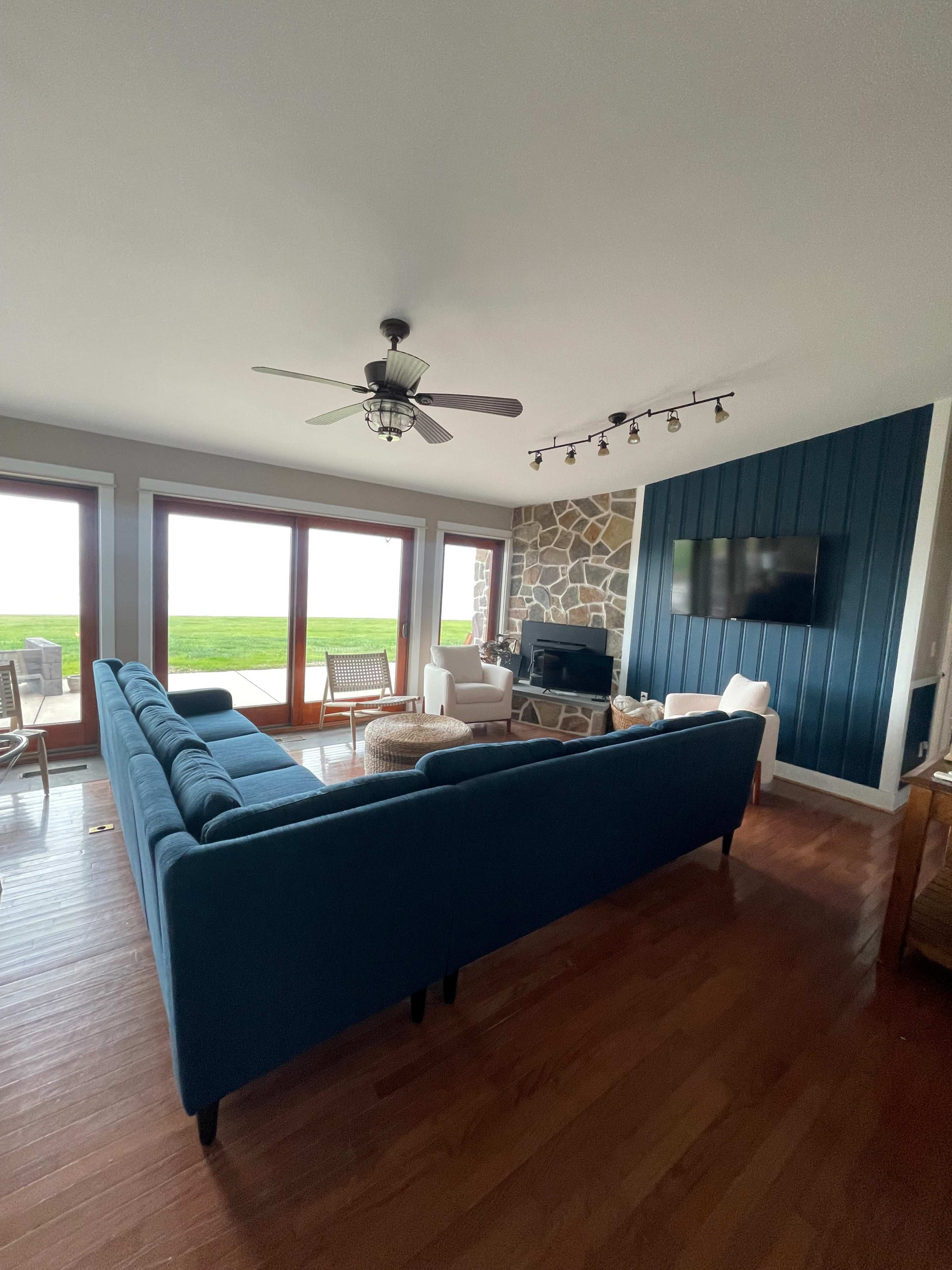 The living room features a blue sofa, a stone accent wall, and large windows with a view of the outdoors.