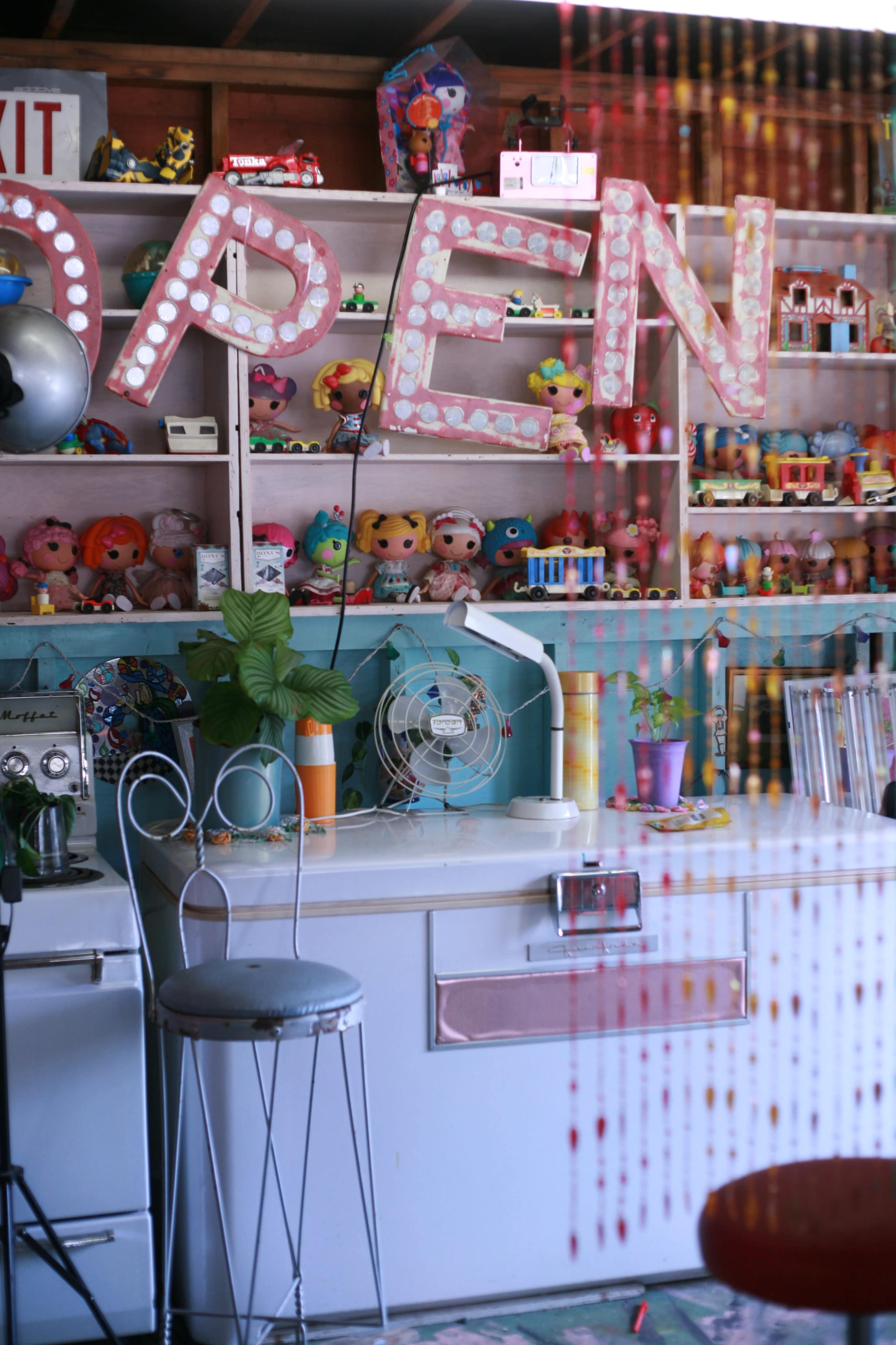 A brightly decorated room filled with vintage toys, an open sign, and various colorful collectibles displayed on shelves.