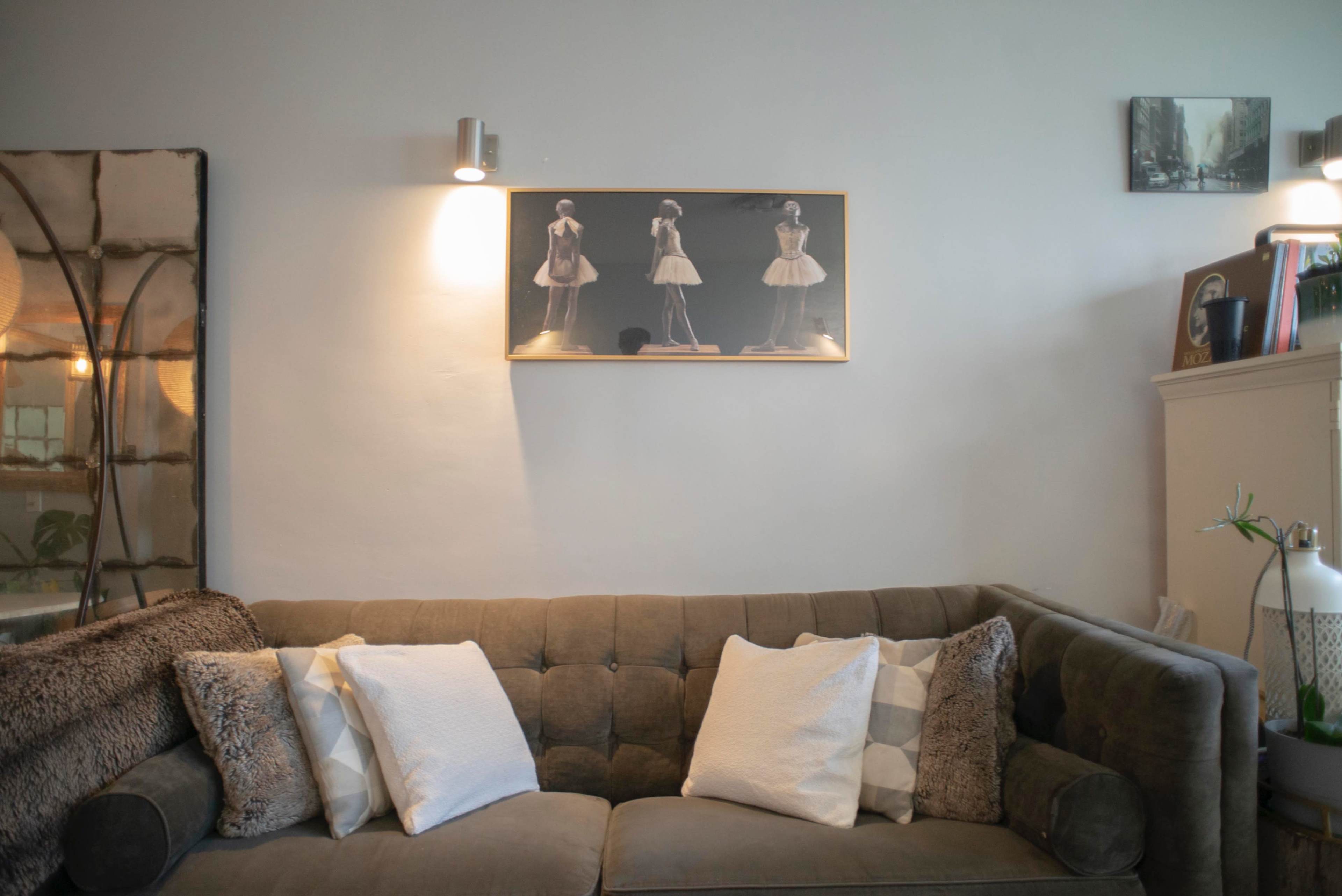 A sectional sofa with two decorative pillows is positioned against a wall featuring framed artwork and wall sconces.