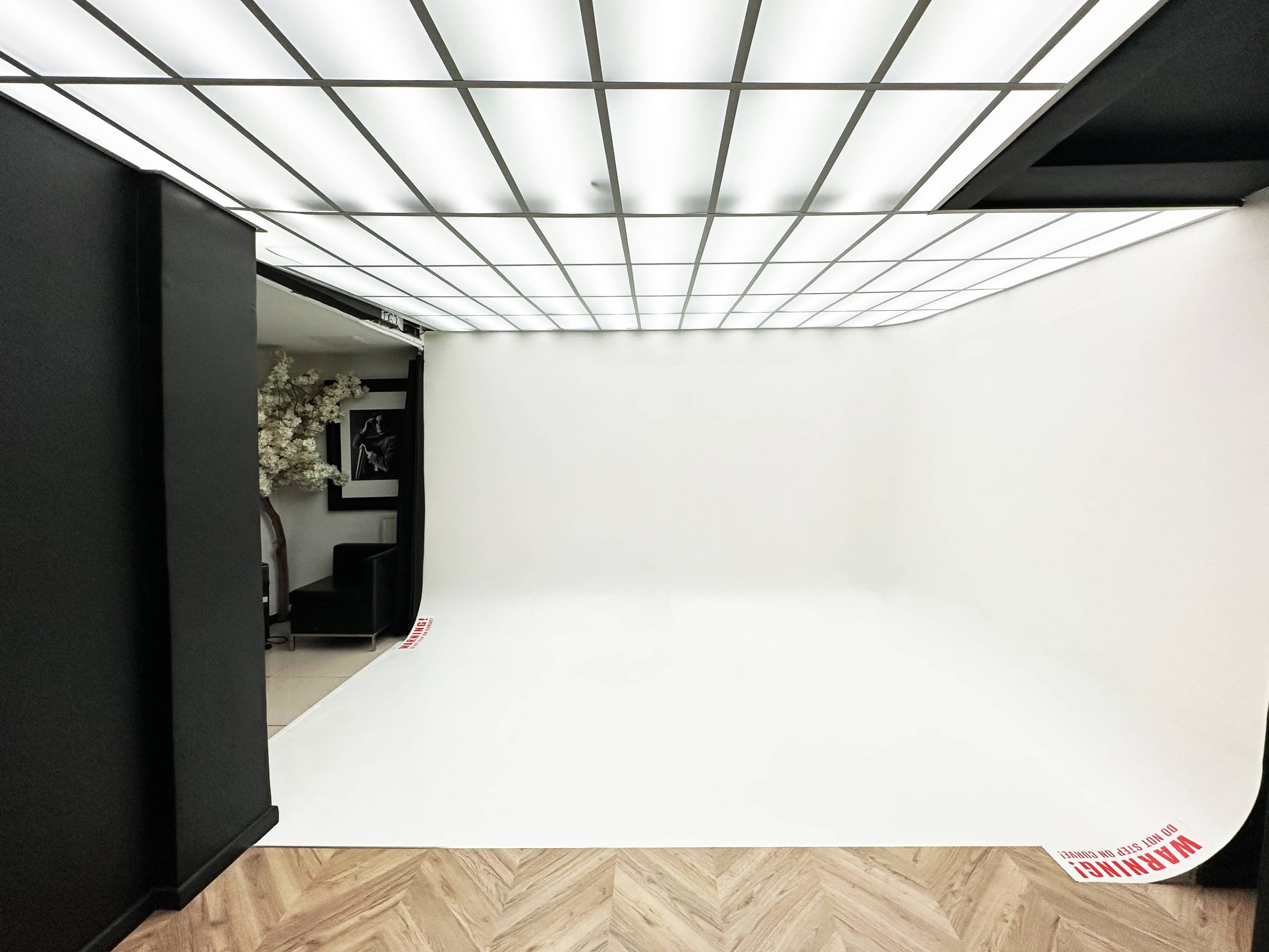 An empty photo studio features a seamless white backdrop and a grid-patterned overhead light.