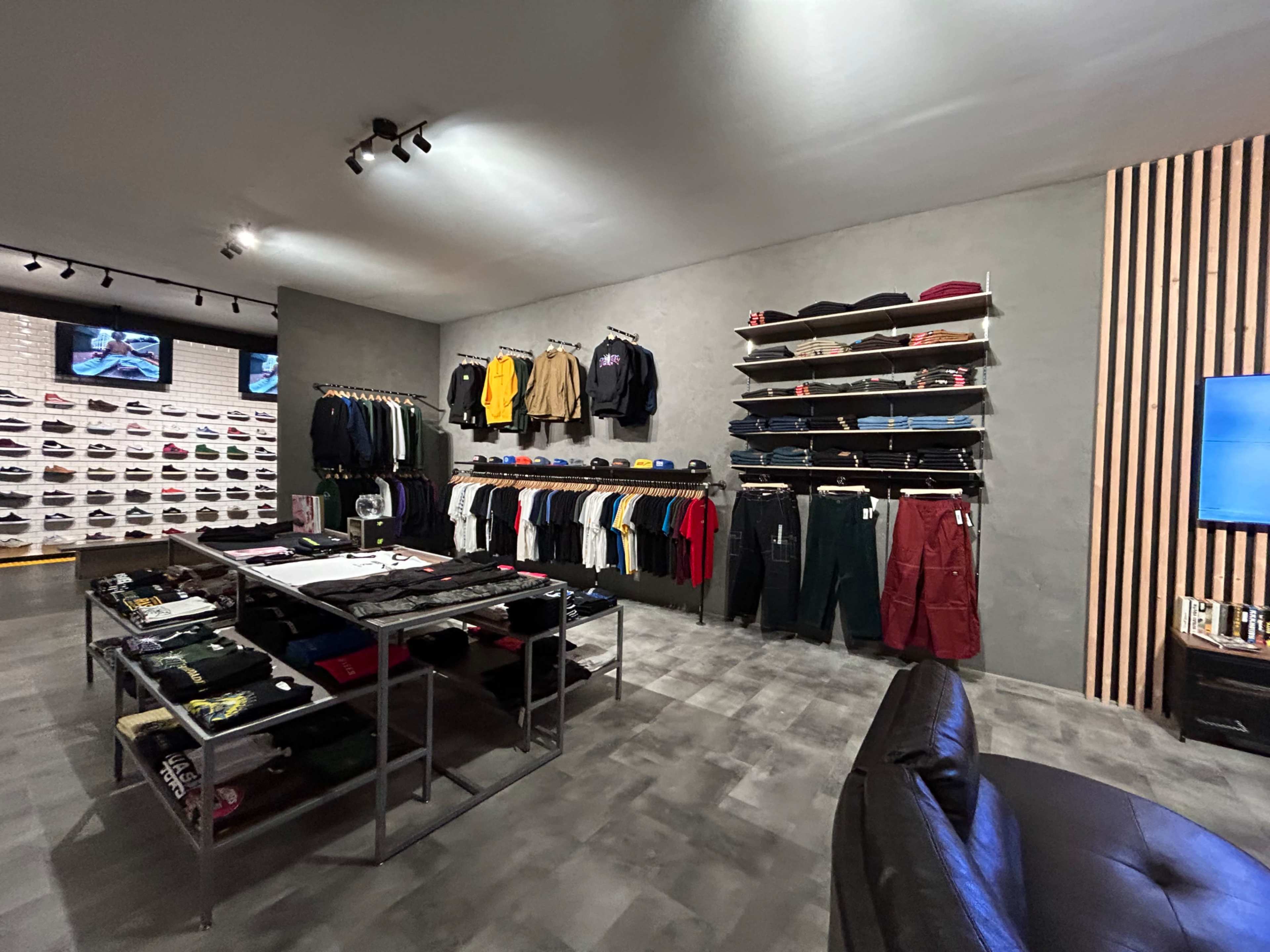 A clothing store interior with racks of apparel and shoes displayed on the walls and a central table with various items for sale.