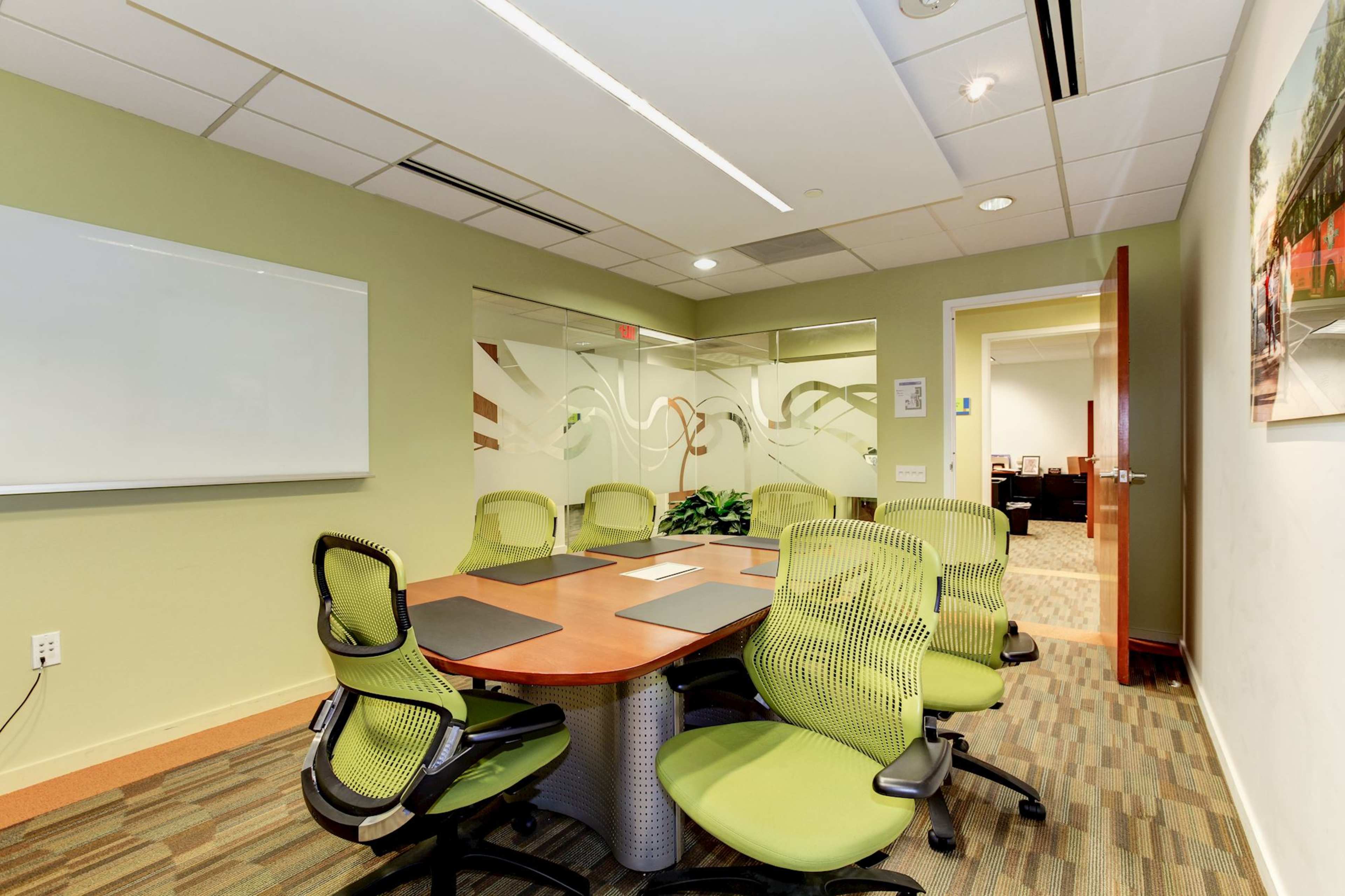 A conference room with a circular table surrounded by green ergonomic chairs and a whiteboard on the wall.