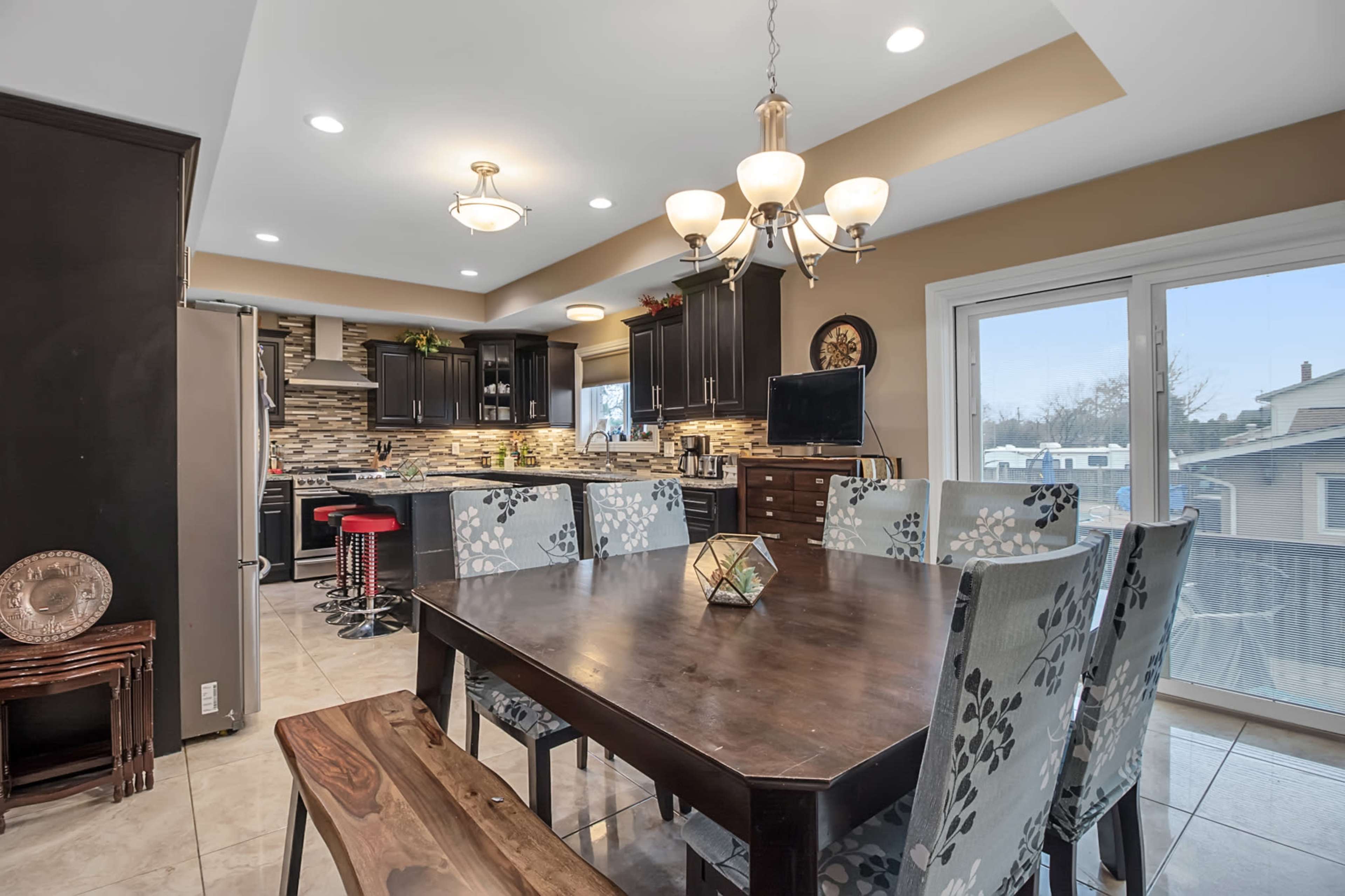 A modern kitchen and dining area features dark cabinetry, a large wooden table, and a sliding glass door leading to an outdoor space.