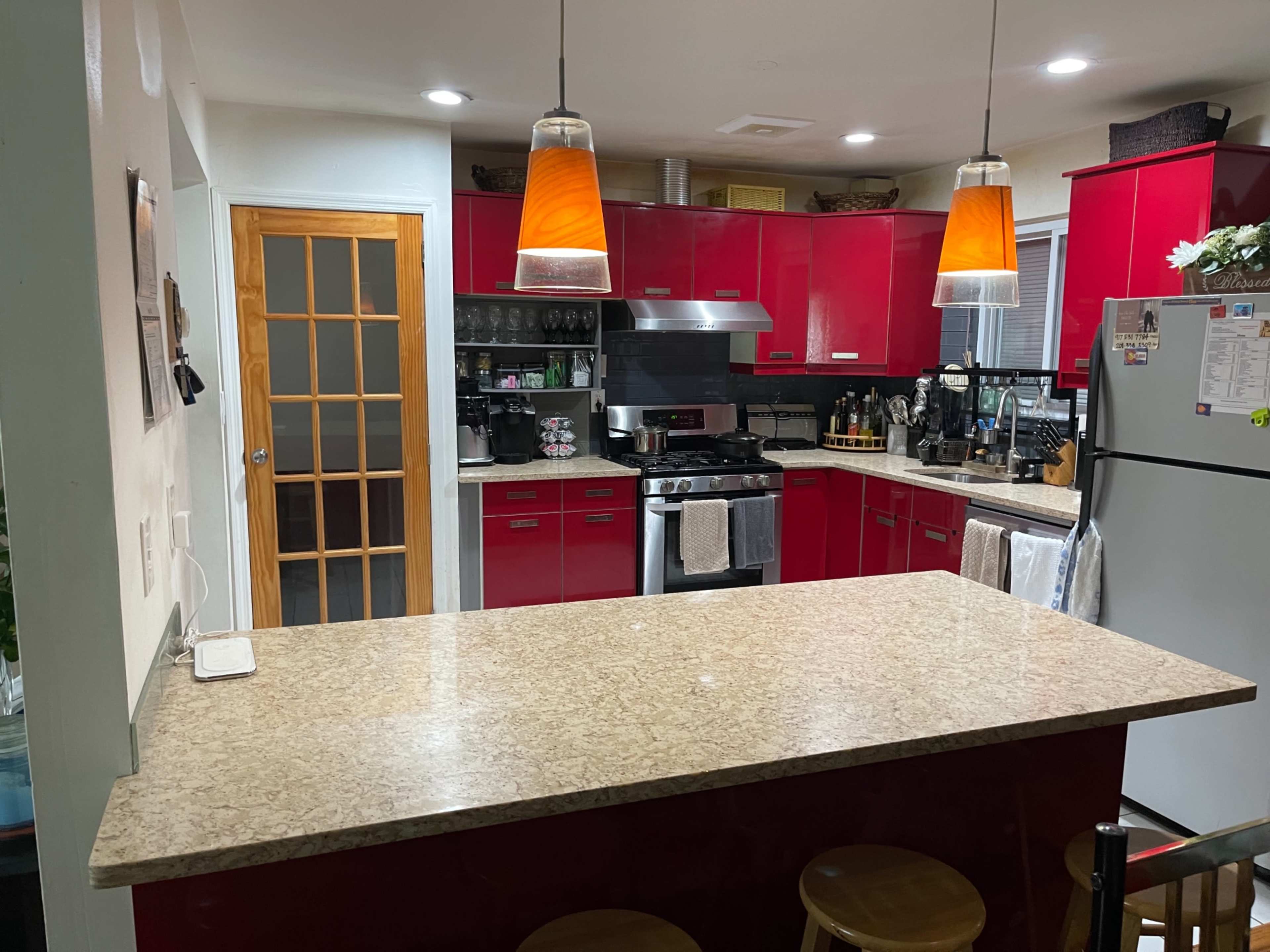 A modern kitchen features red cabinets, a granite countertop, and pendant lighting above the bar area.