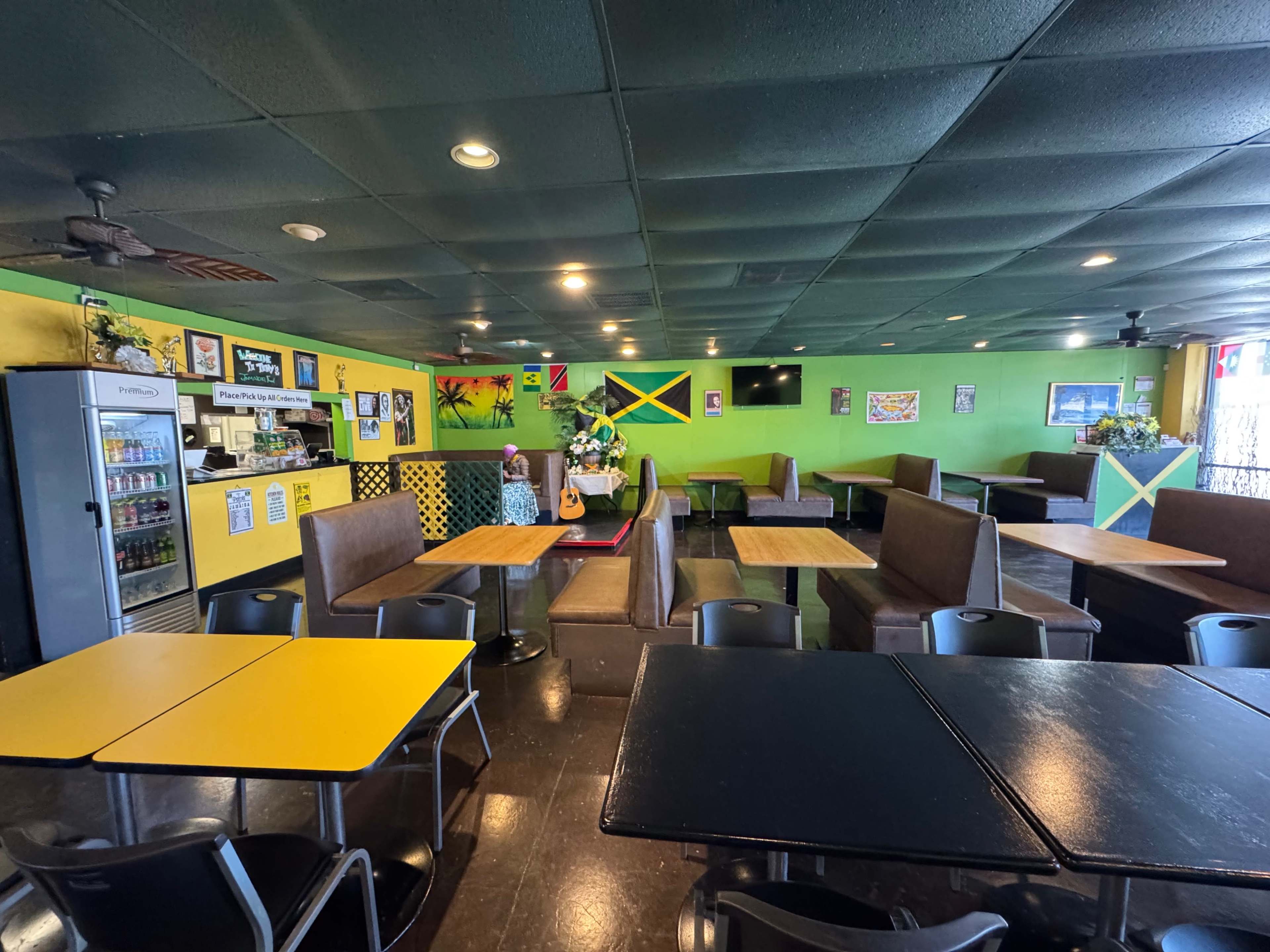 The image shows the interior of a restaurant decorated with bright green walls, wooden tables, and Jamaican-themed artwork.