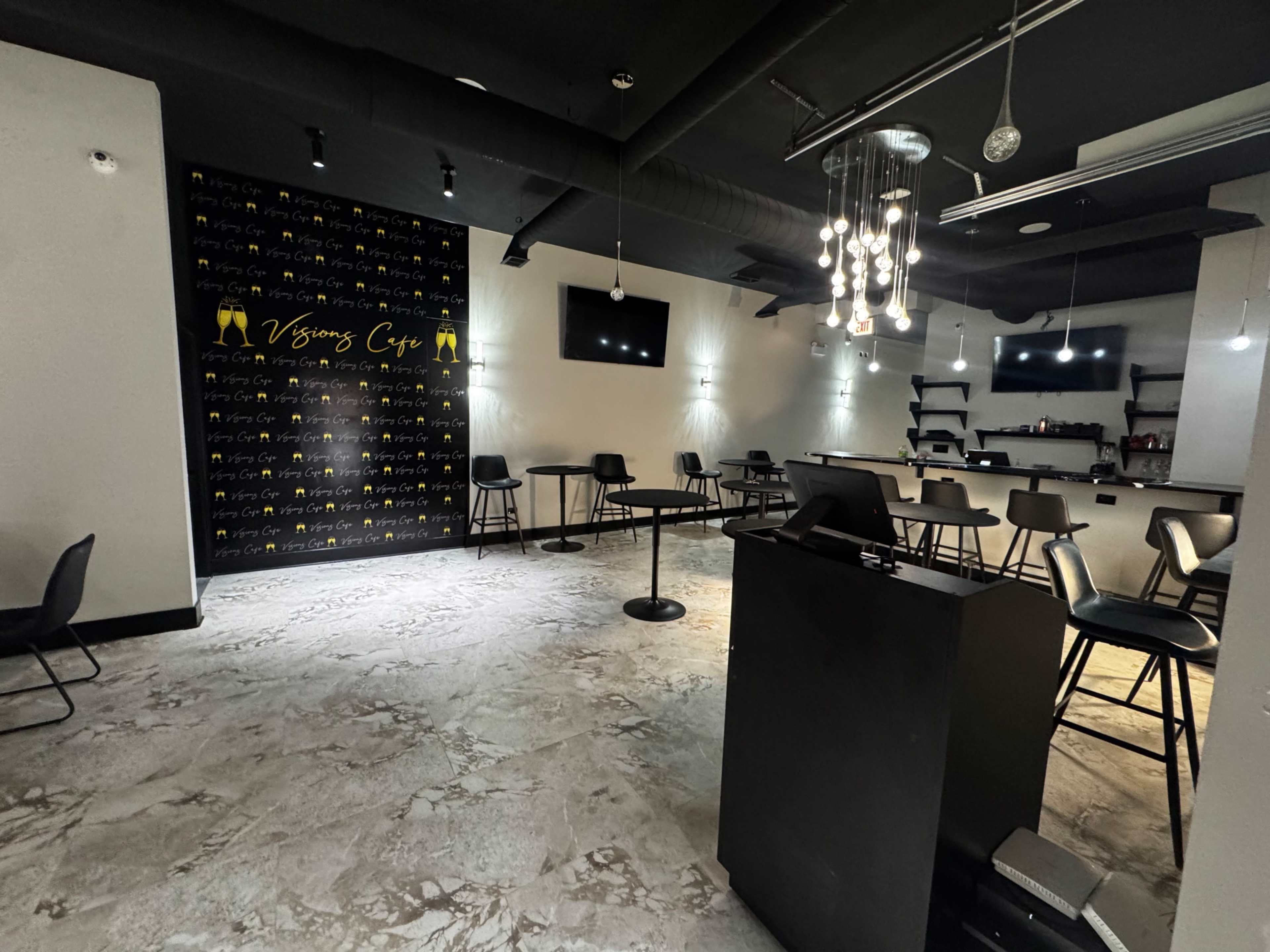 The image shows a modern cafe interior with black chairs, a bar area, and a decorative wall featuring the name "Vision's Cafe" in yellow.