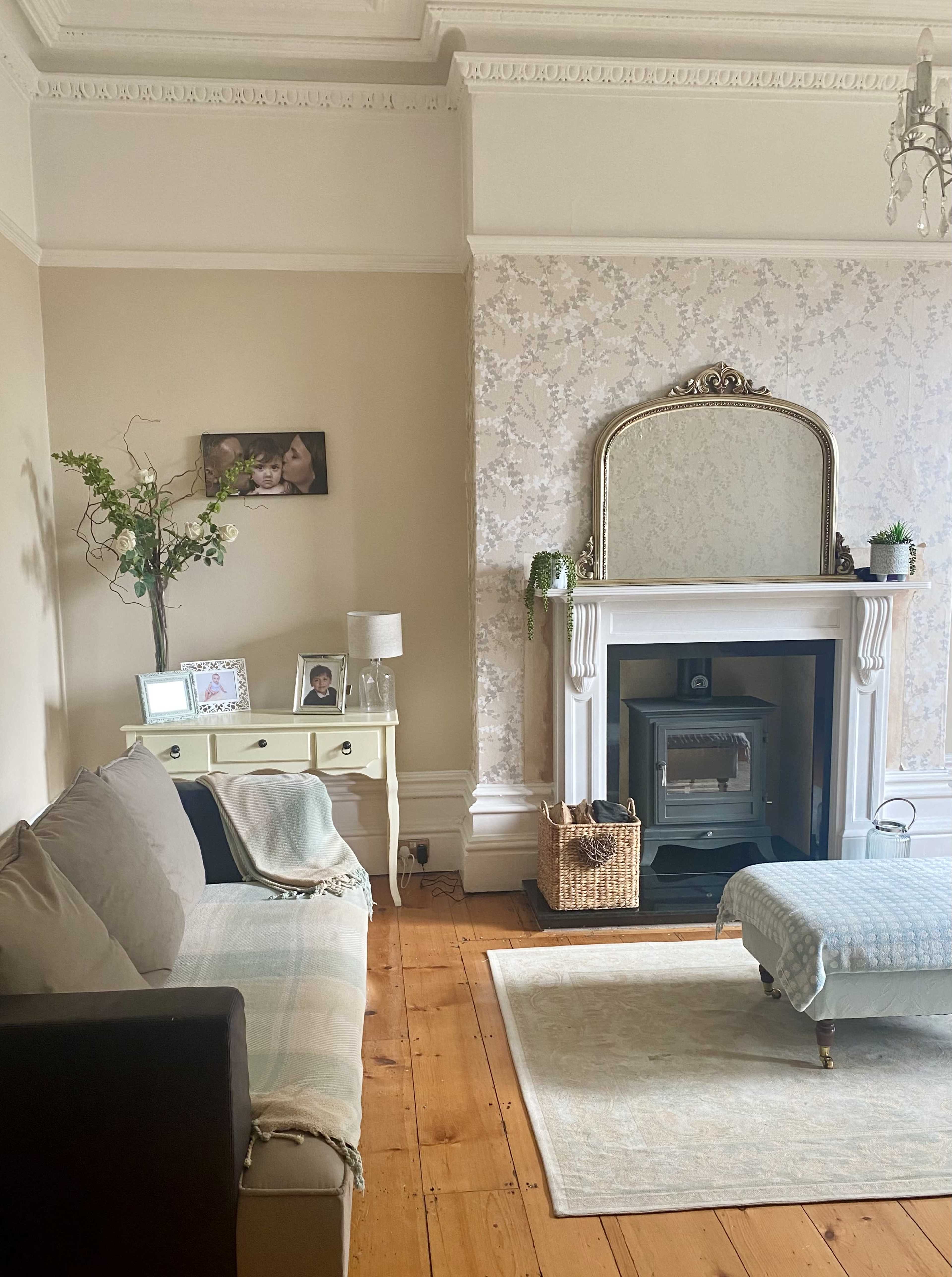 The living room features a beige sofa, a decorative fireplace with a mirror, a wooden floor, and a small coffee table.
