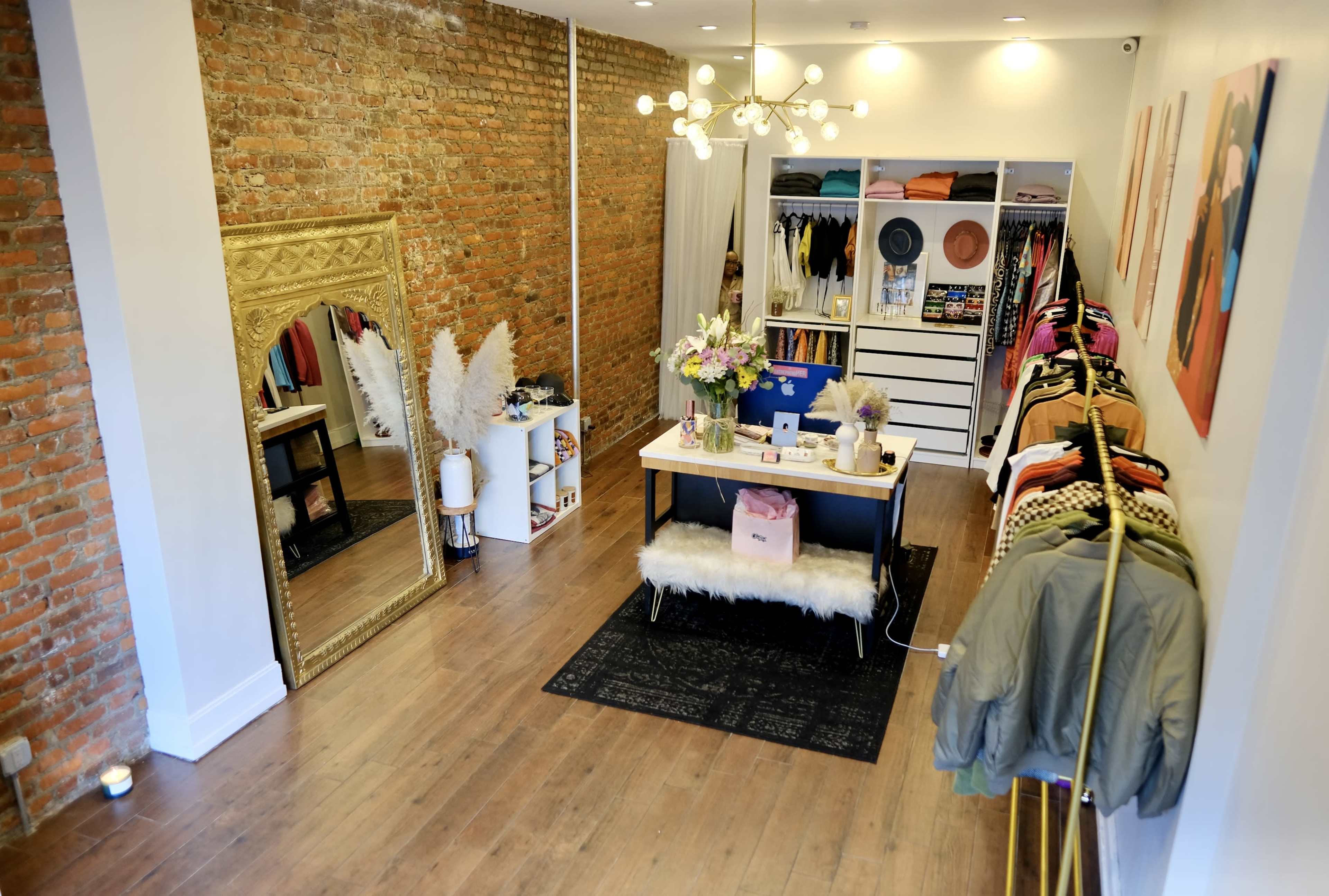A boutique featuring exposed brick walls, a large mirror, clothing racks, and a central display table with flowers.