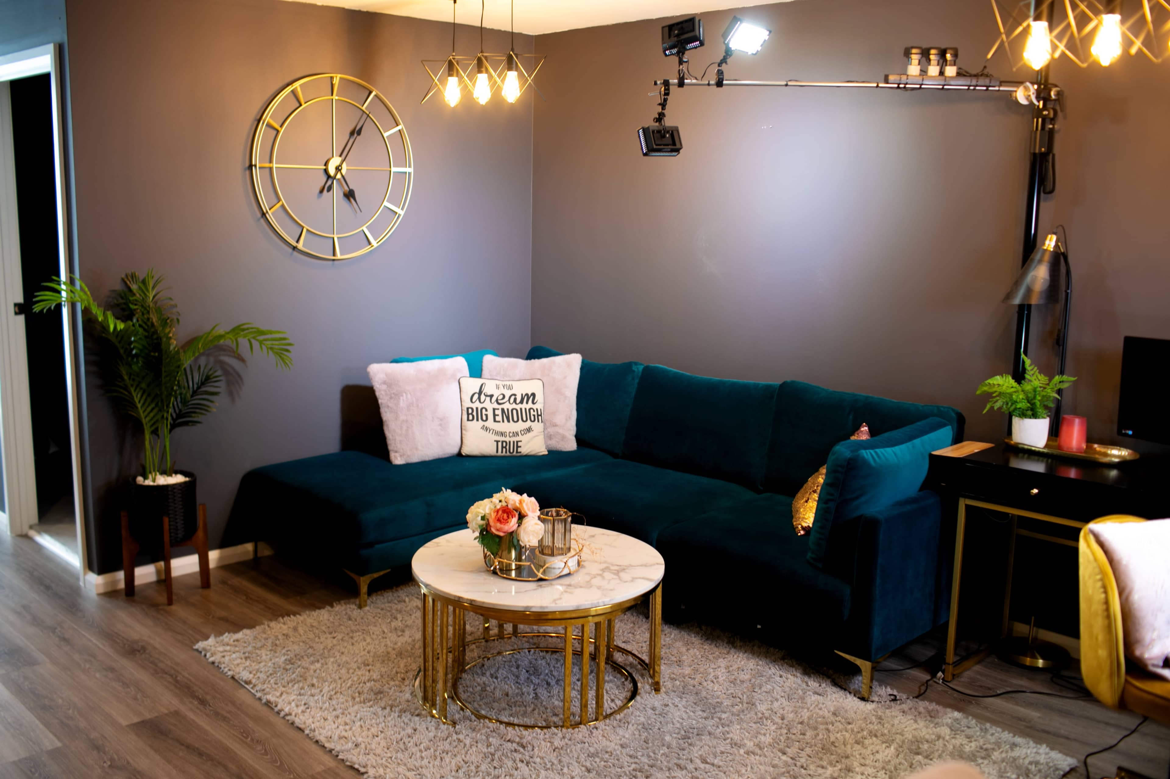 A cozy living room featuring a dark green sectional sofa, a round marble coffee table, and decorative elements like a clock and potted plants against a gray wall.