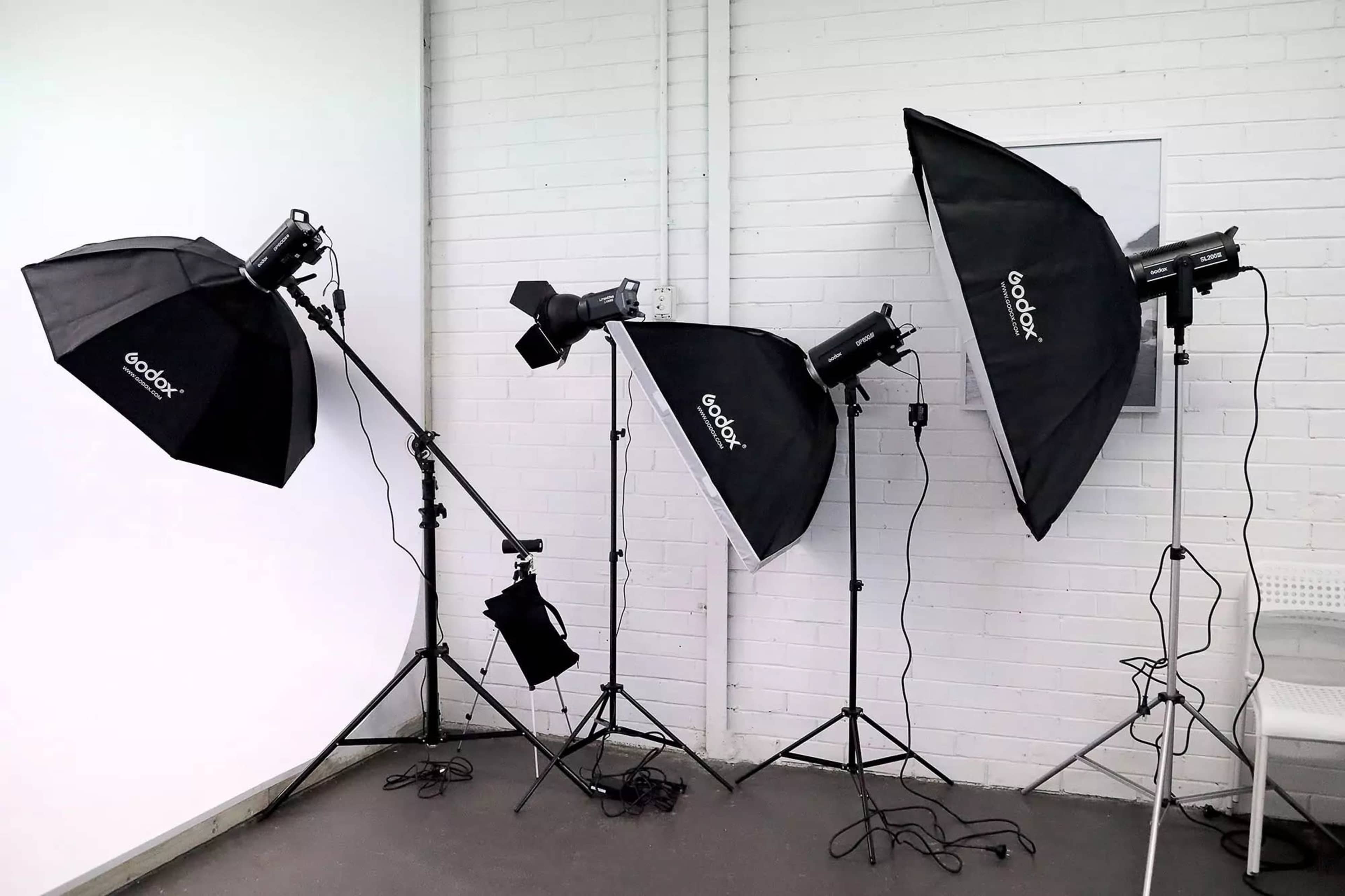 Three Godox studio lights with softboxes are arranged on stands against a white brick wall in a photography studio.