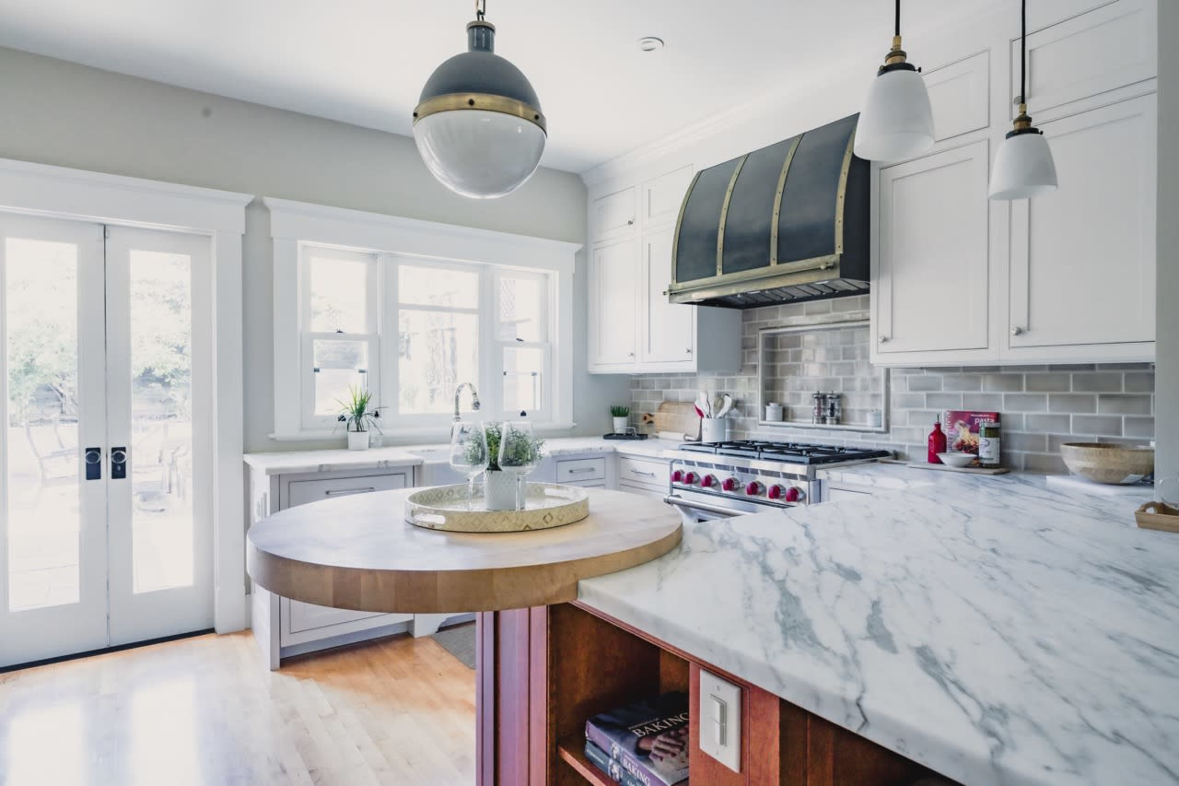 A modern kitchen features sleek white cabinetry, a marble countertop island, and a stainless steel range hood.
