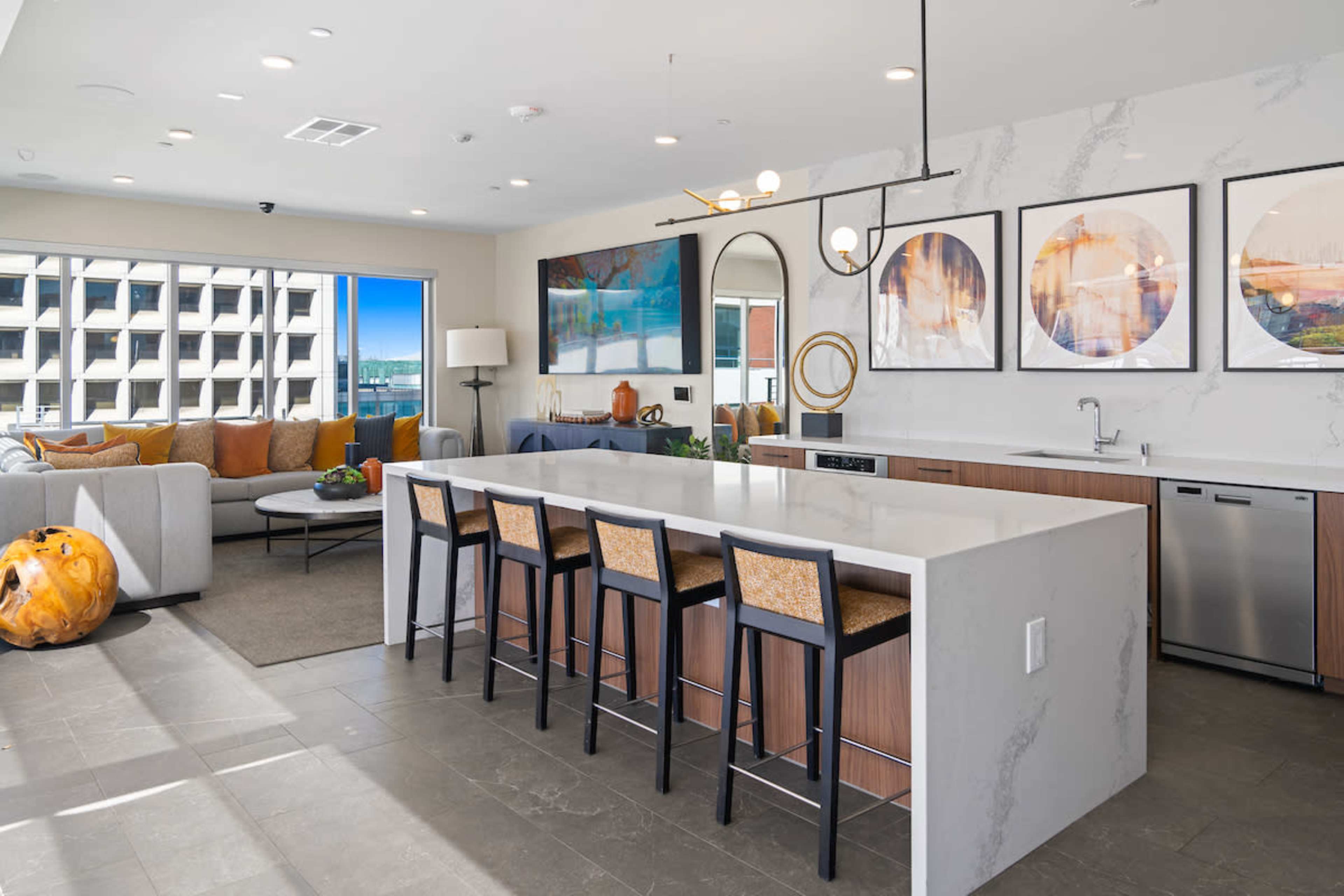 The image shows a modern kitchen area with a large island, bar stools, and large windows overlooking a cityscape.
