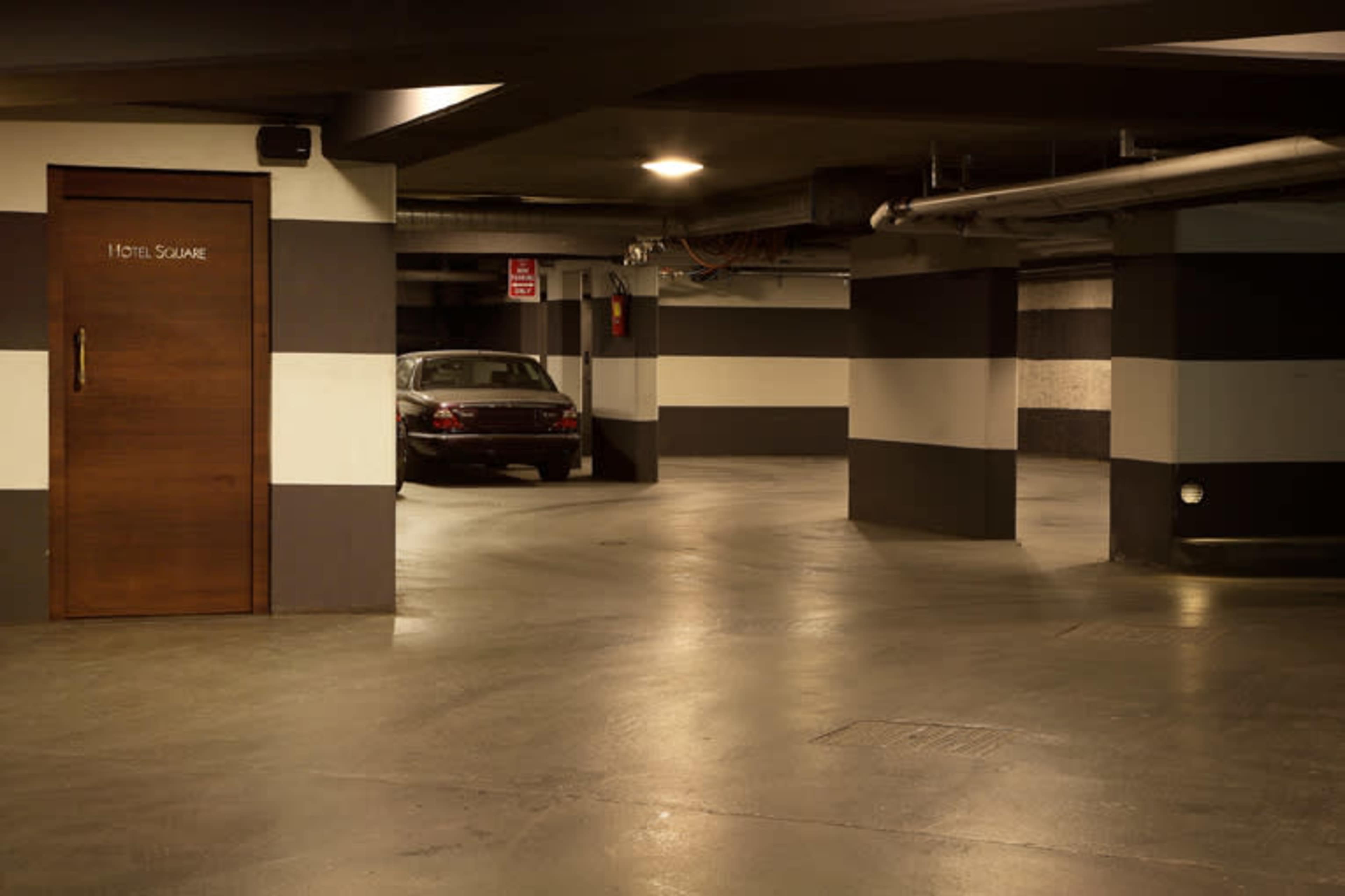 A dimly lit underground parking garage with striped walls and a parked car near a door labeled "HOTEL SQUARE."