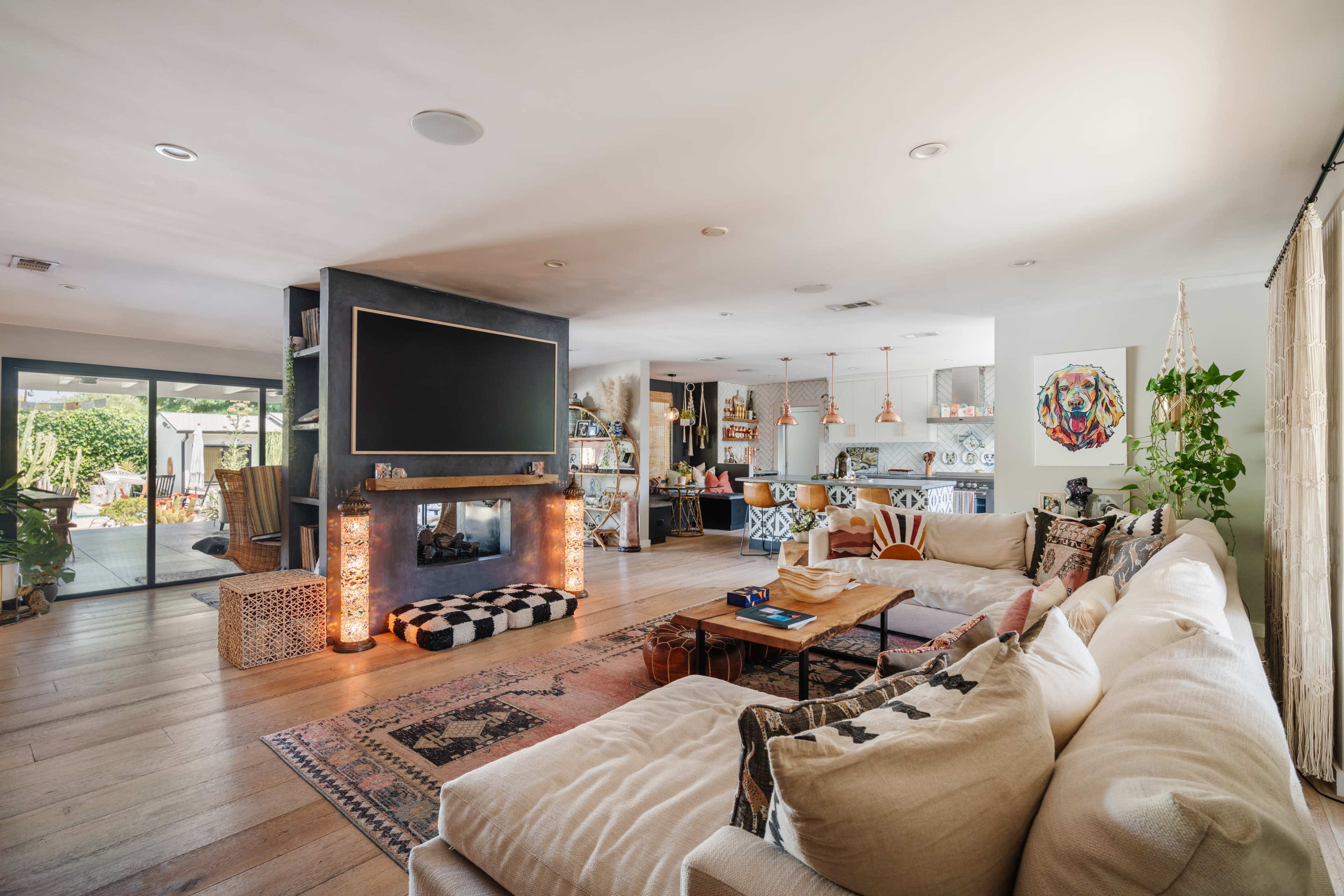 A spacious living room with a large television mounted on the wall, a cozy sectional sofa, and an open kitchen area visible in the background.