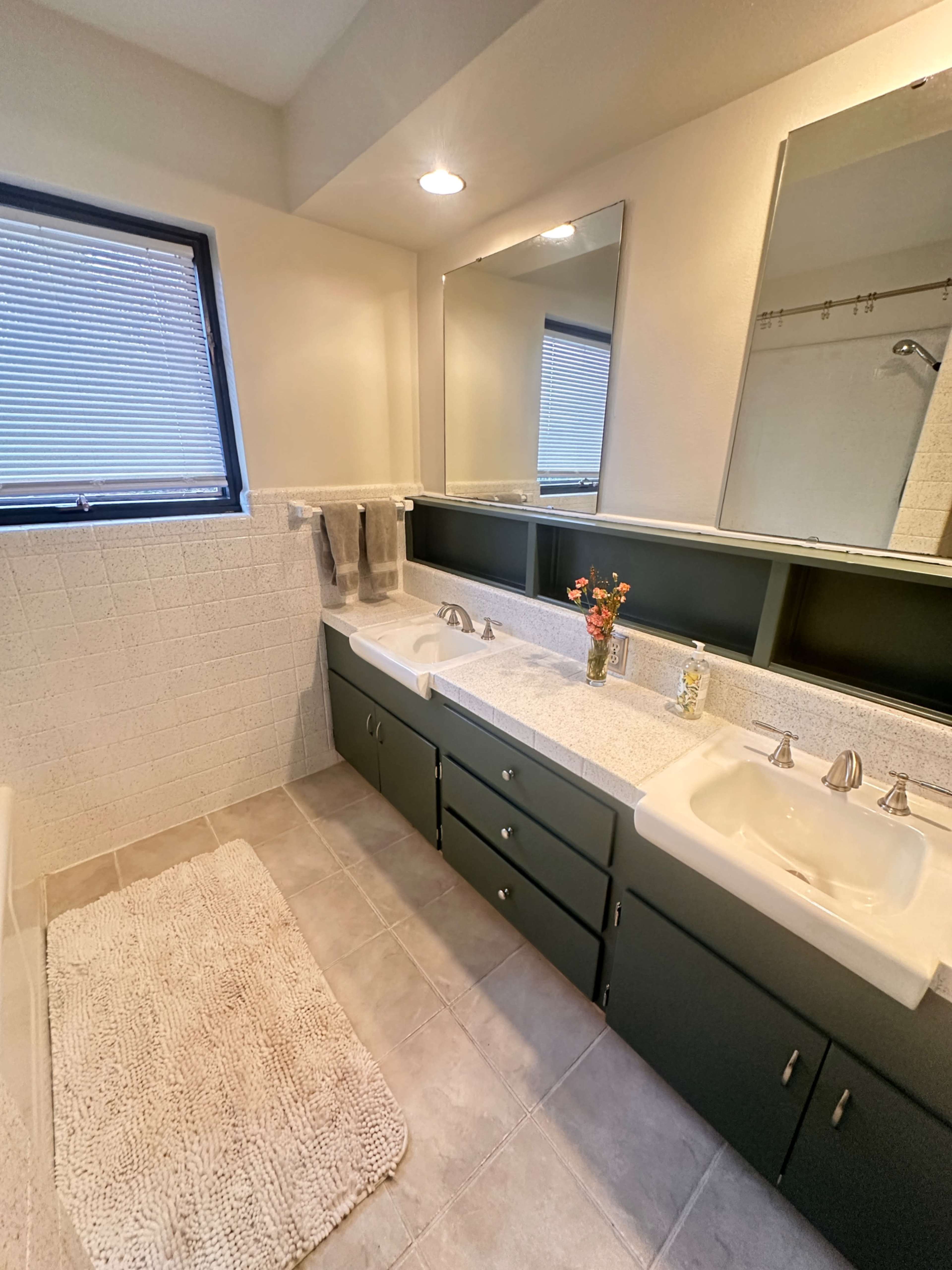 The bathroom features dual sinks with a mirror above, dark cabinetry, and a light tile floor.