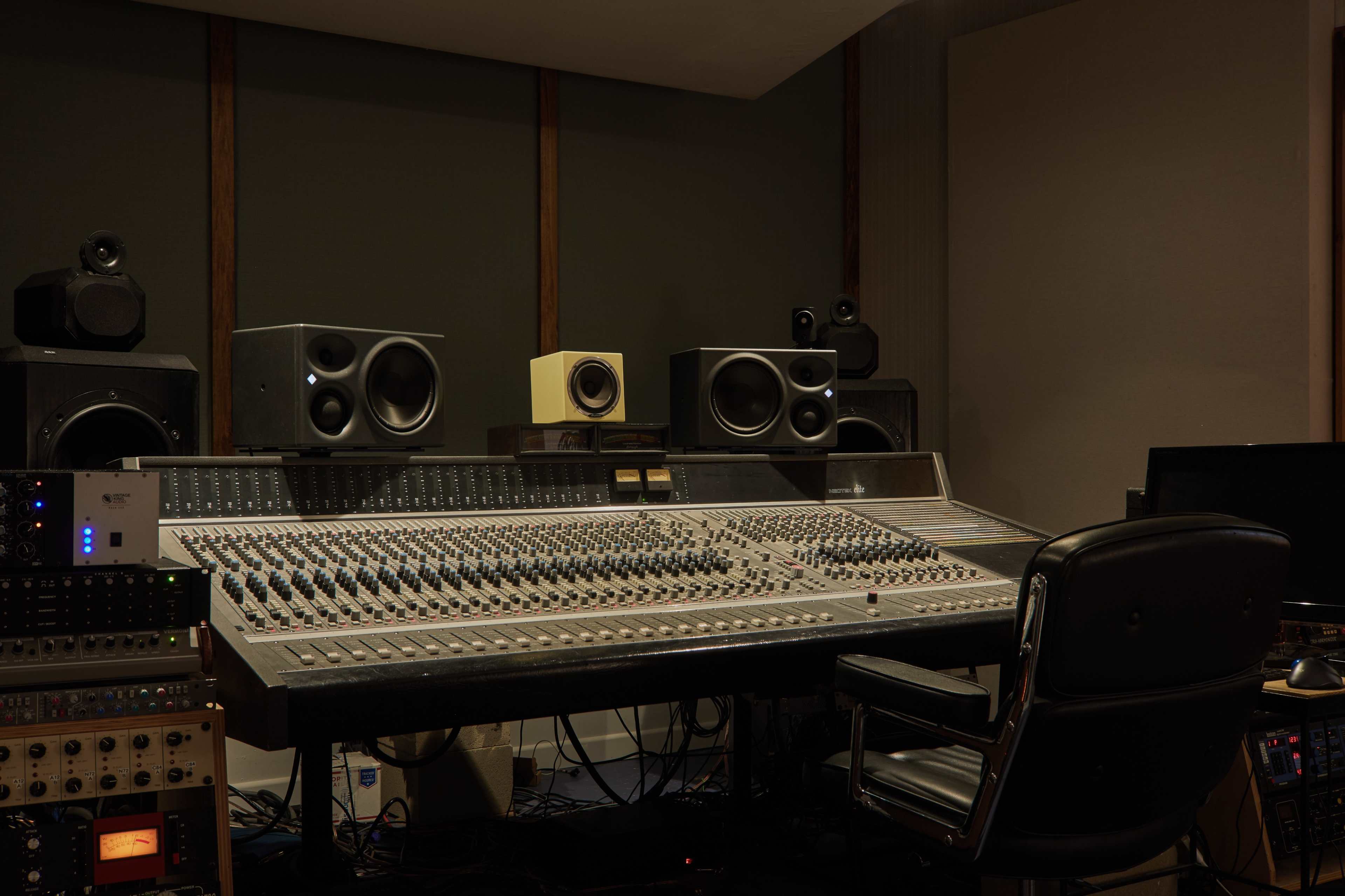 A recording studio features a large mixing console surrounded by speakers and audio equipment.