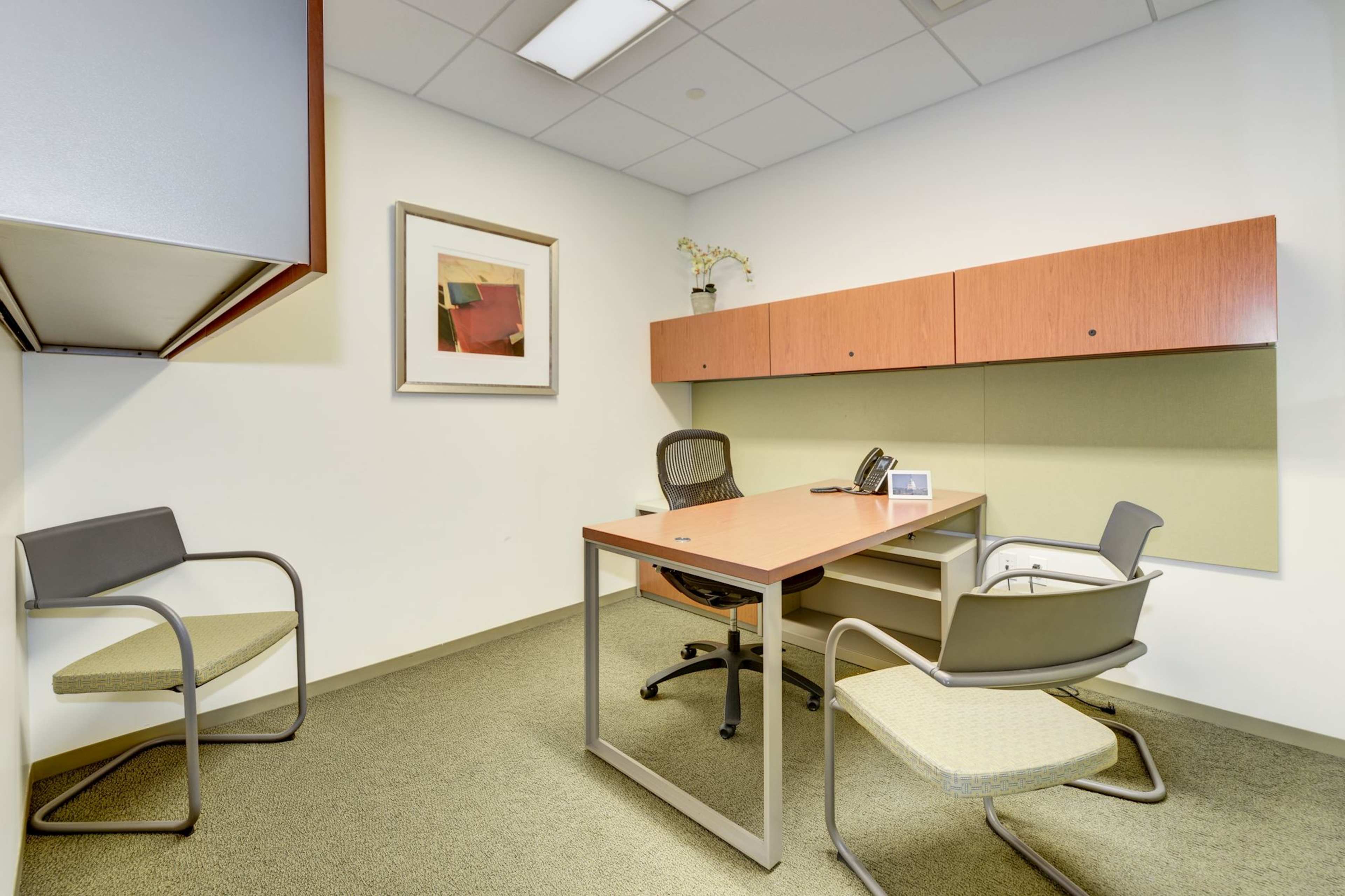A small office space with a wooden desk, two chairs, a phone, and wall-mounted cabinets.