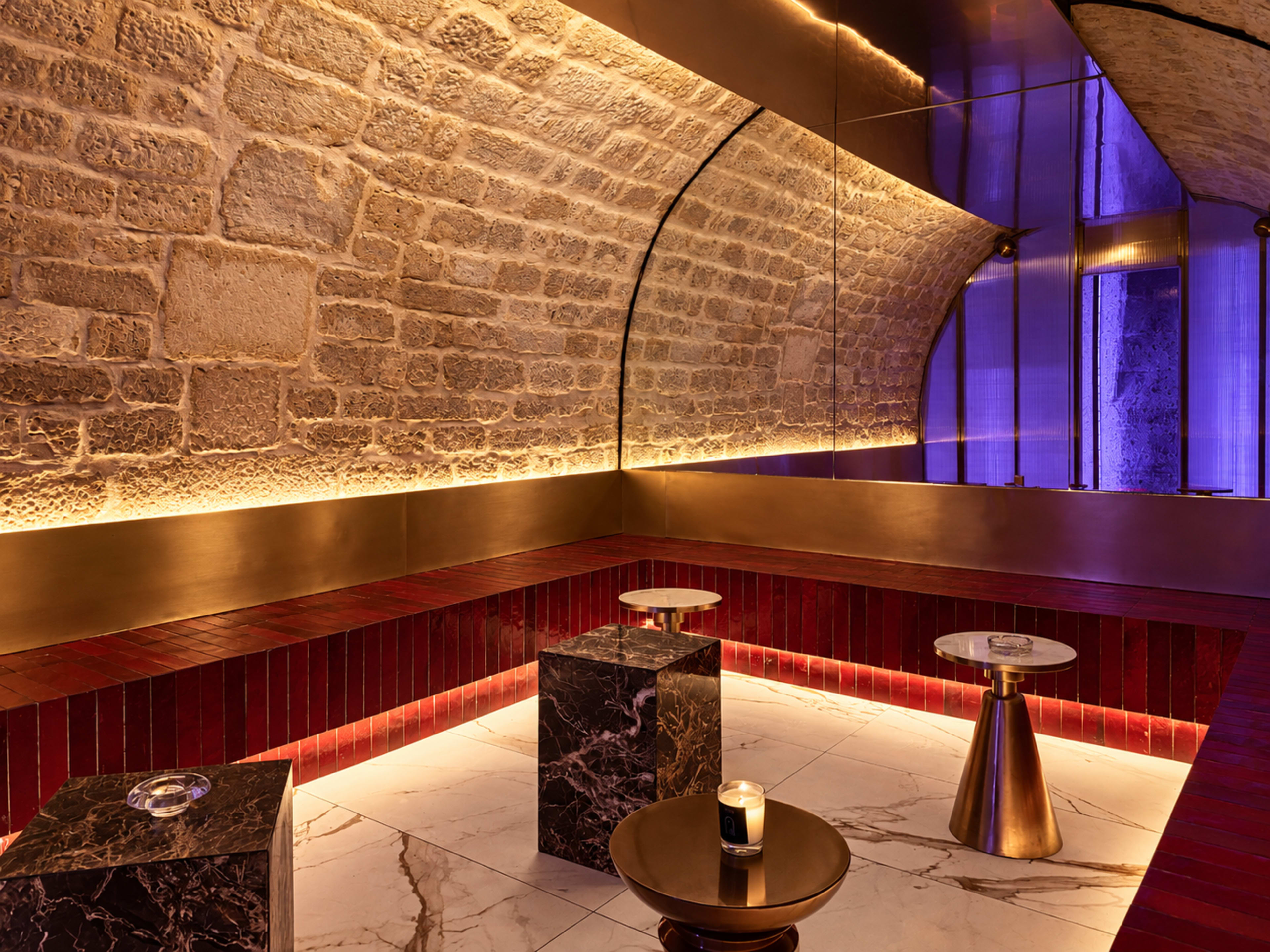 The image depicts a modern, stylish lounge area featuring stone walls, polished surfaces, and minimalist furniture with soft lighting.