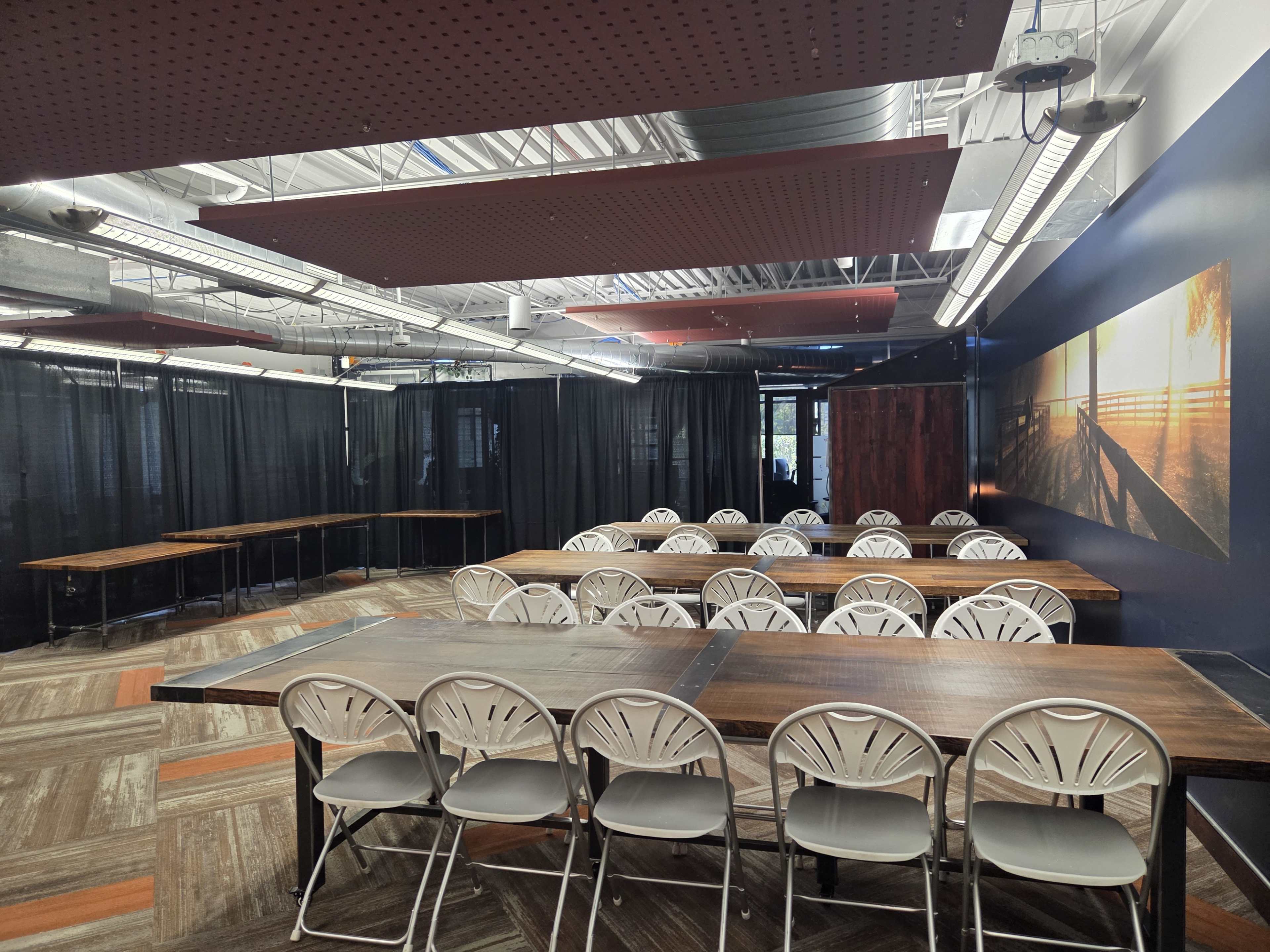 The image shows a room arranged with several tables and chairs, featuring a dark wall with a large photograph and draped black fabric partitions.
