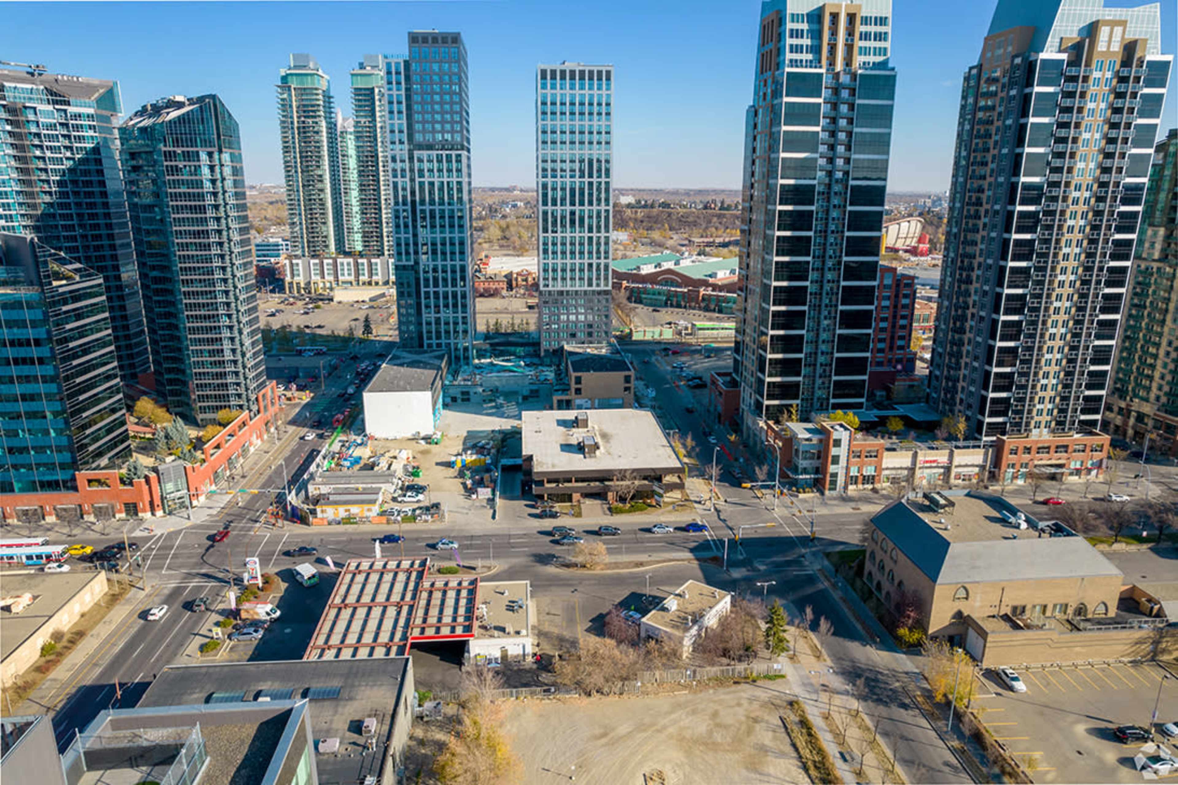 The image shows a skyline of modern skyscrapers with a construction lot and intersecting streets in an urban setting.