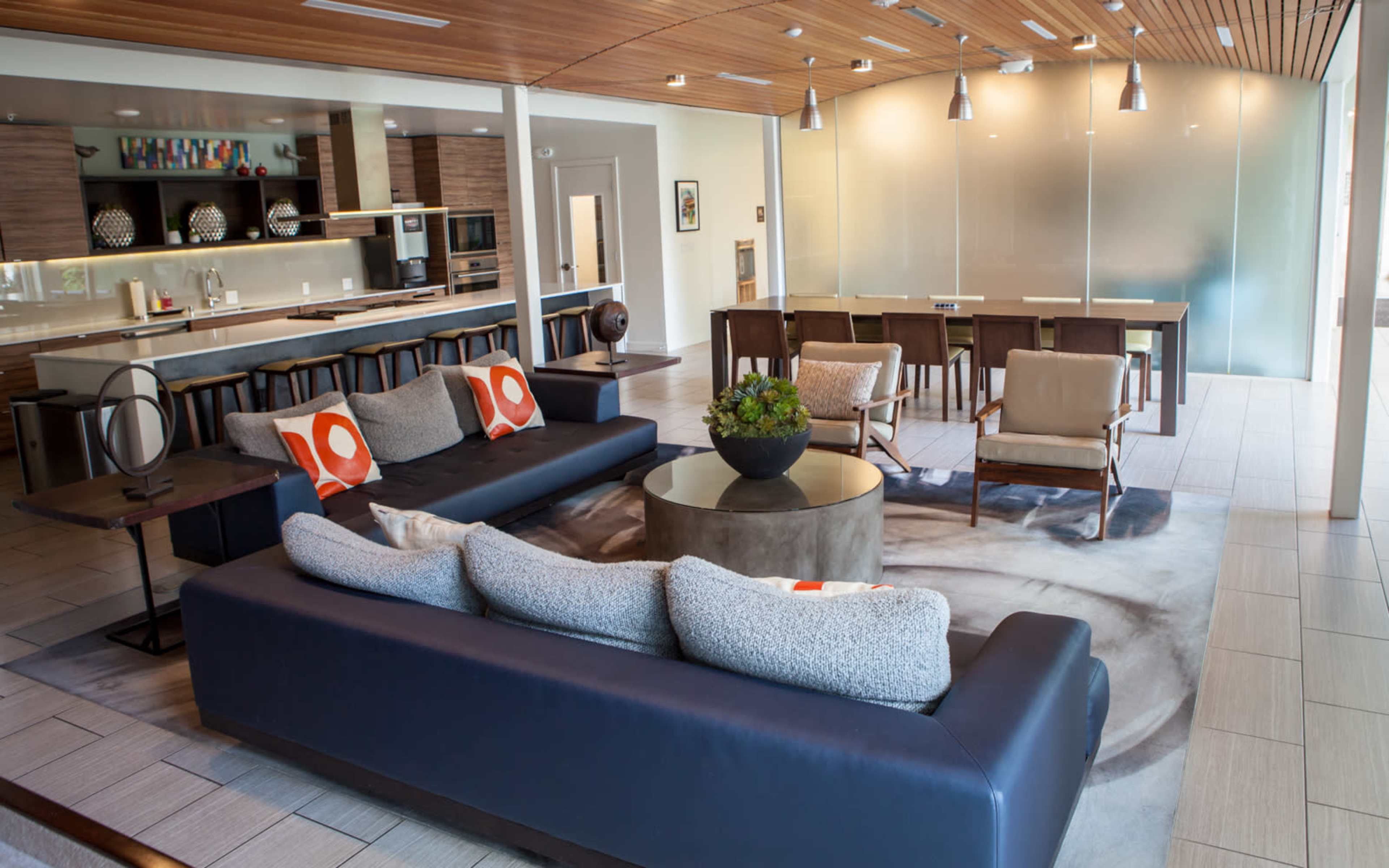 A modern living area featuring a sectional couch, a coffee table, and a dining area in the background with a kitchen.