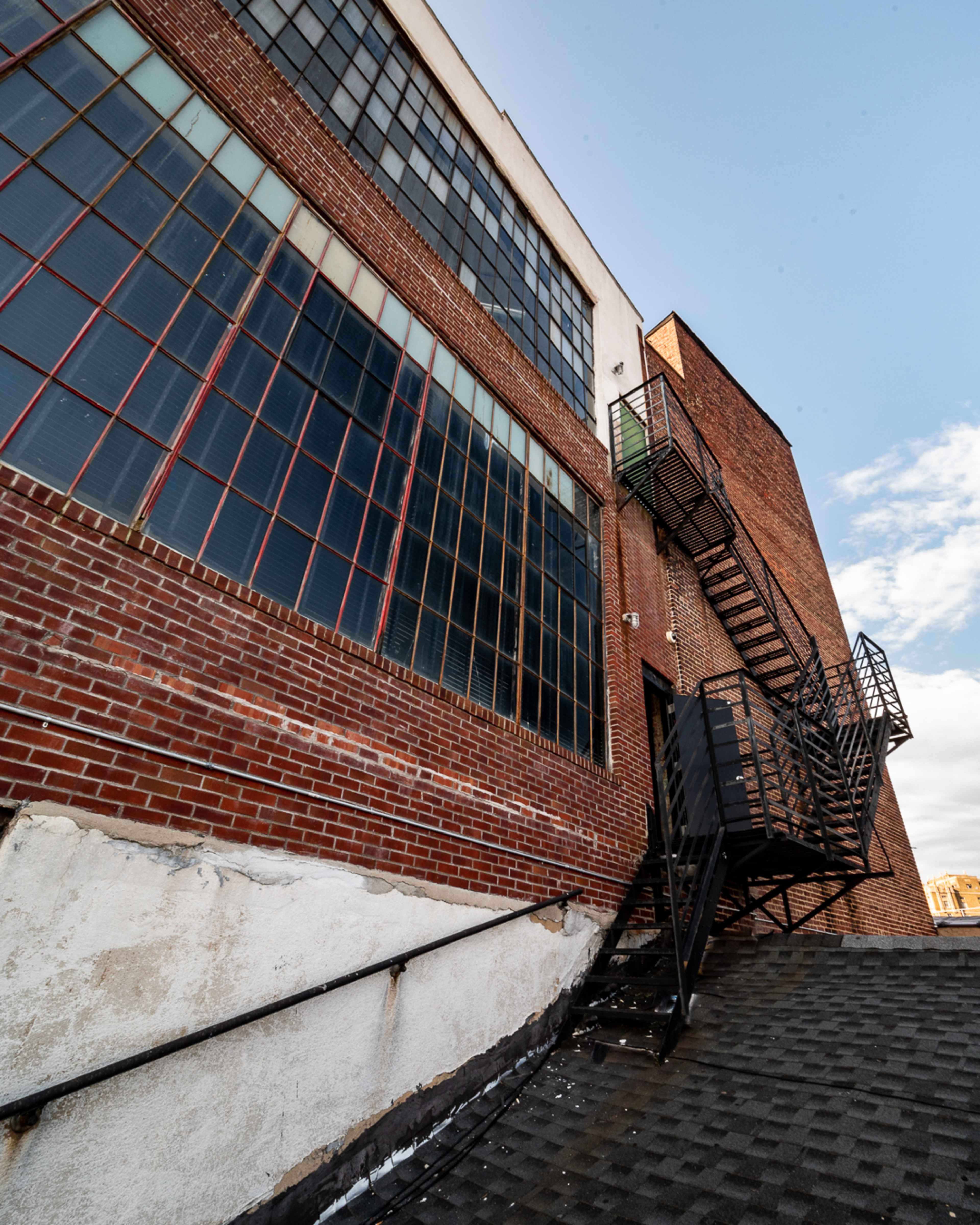 The image shows a brick building with large windows and an external metal fire escape.