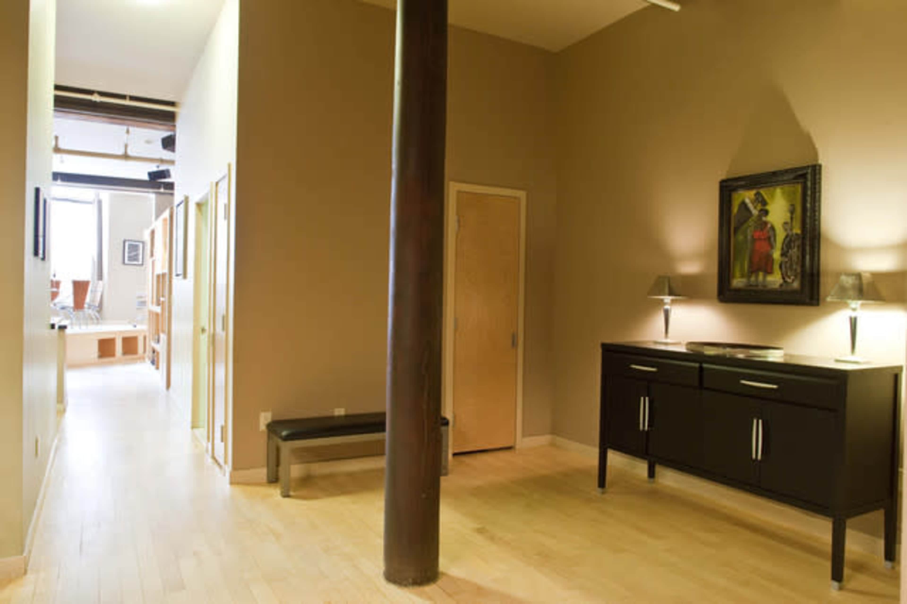 A modern interior space with hardwood floors, a dark wood cabinet, a framed painting on the wall, and a hallway leading to other rooms.