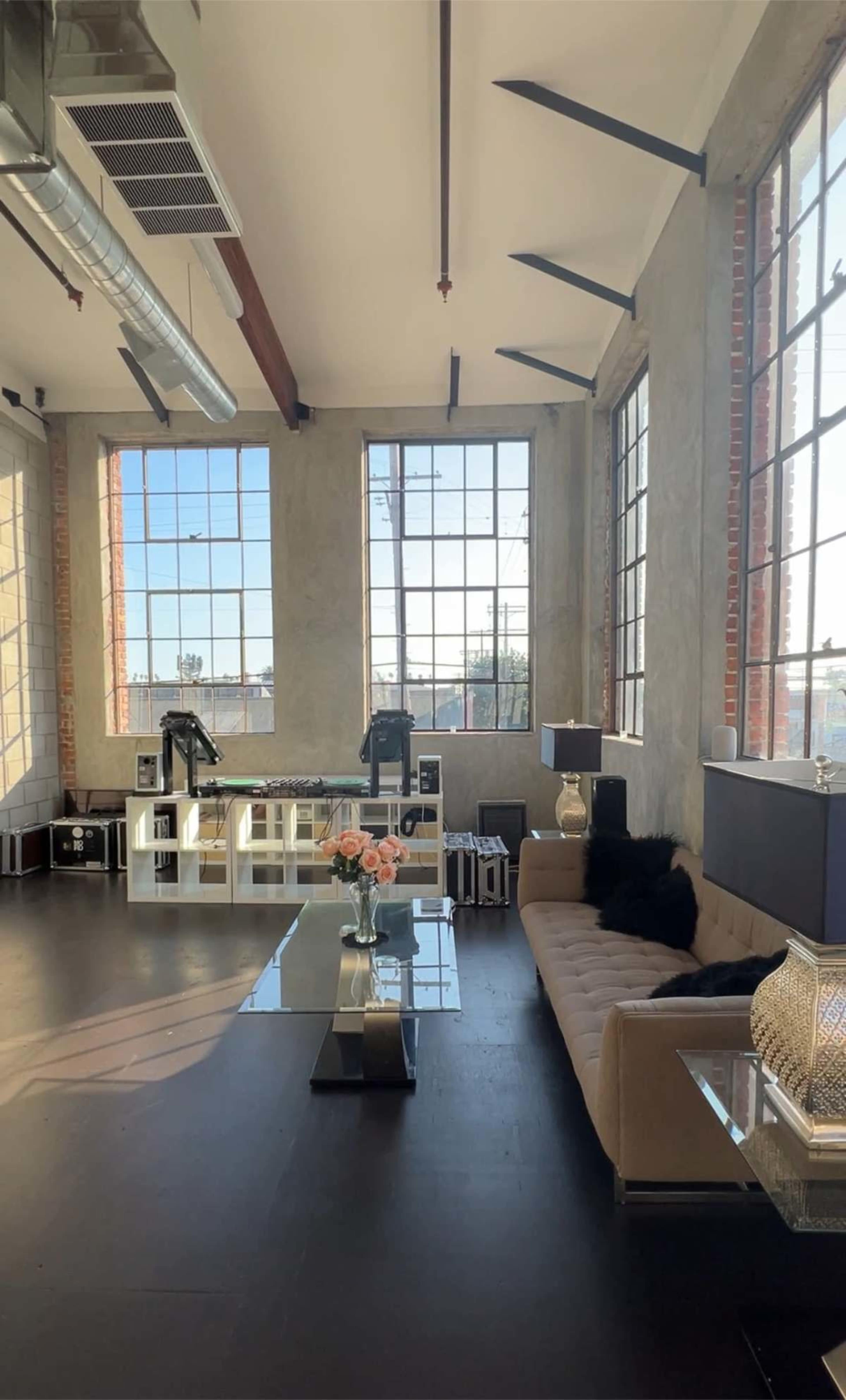 The image shows a spacious, modern interior with large windows, featuring a sofa, glass coffee table, and decorative elements.