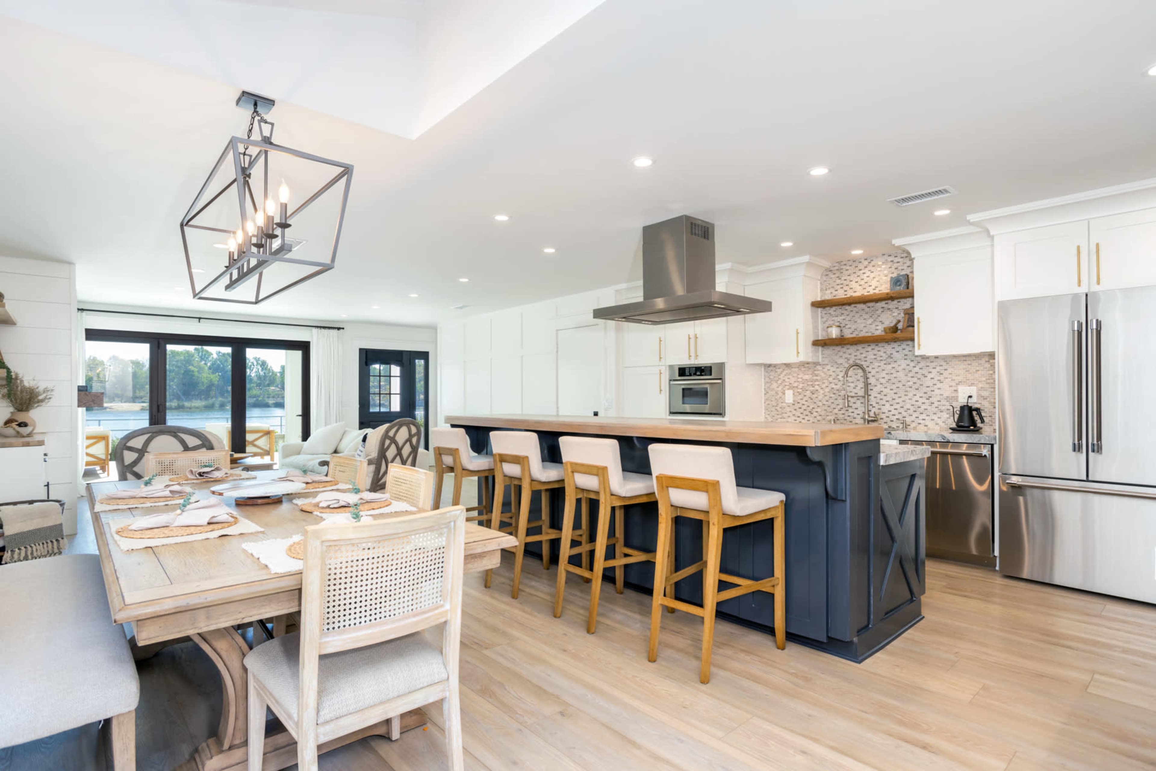 A modern kitchen and dining area feature a large island with bar seating, stainless steel appliances, and a table set for a meal.