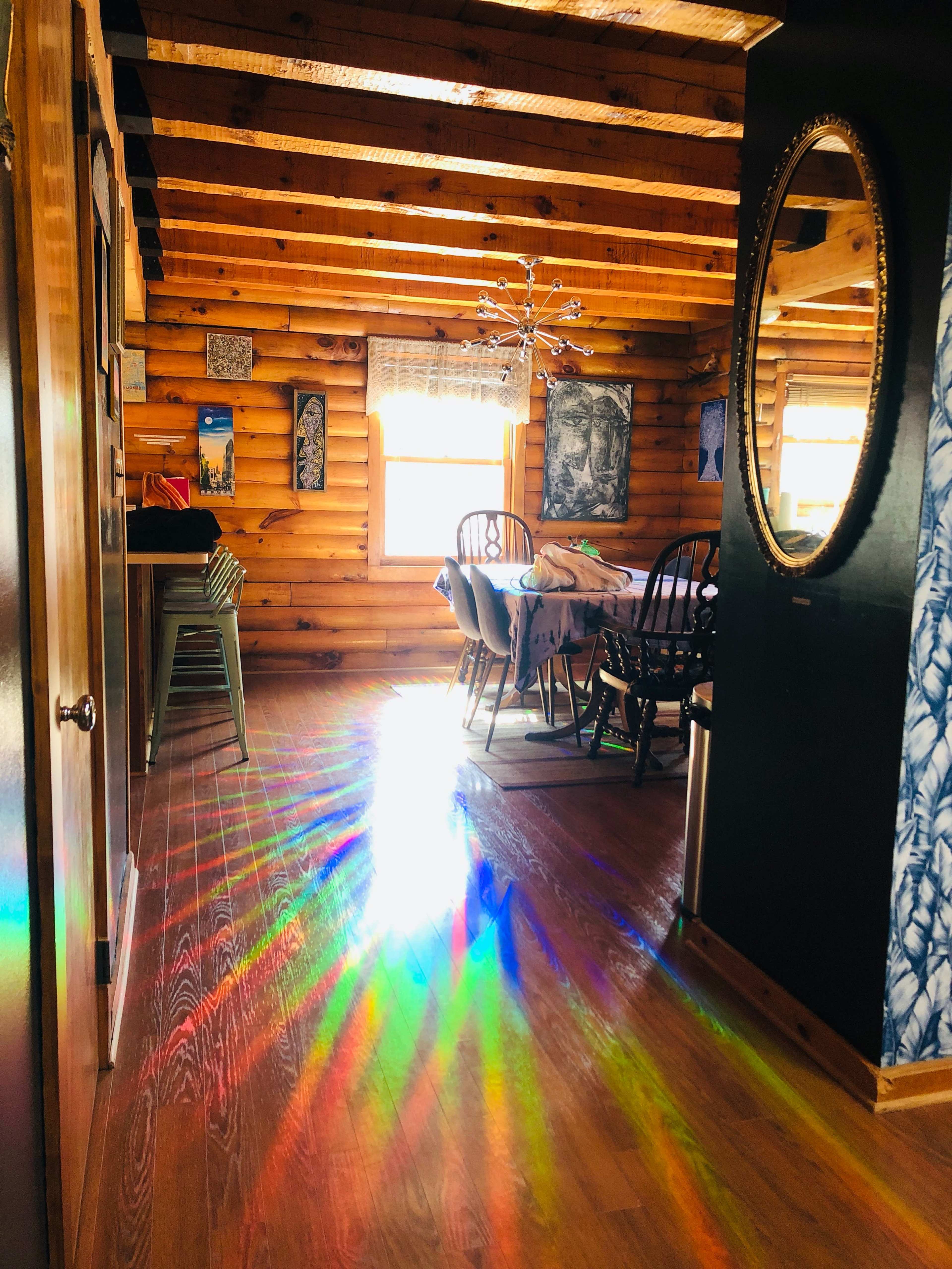 Sunlight creates a spectrum of colors on the wooden floor of a log cabin, illuminating the dining area and surrounding decor.