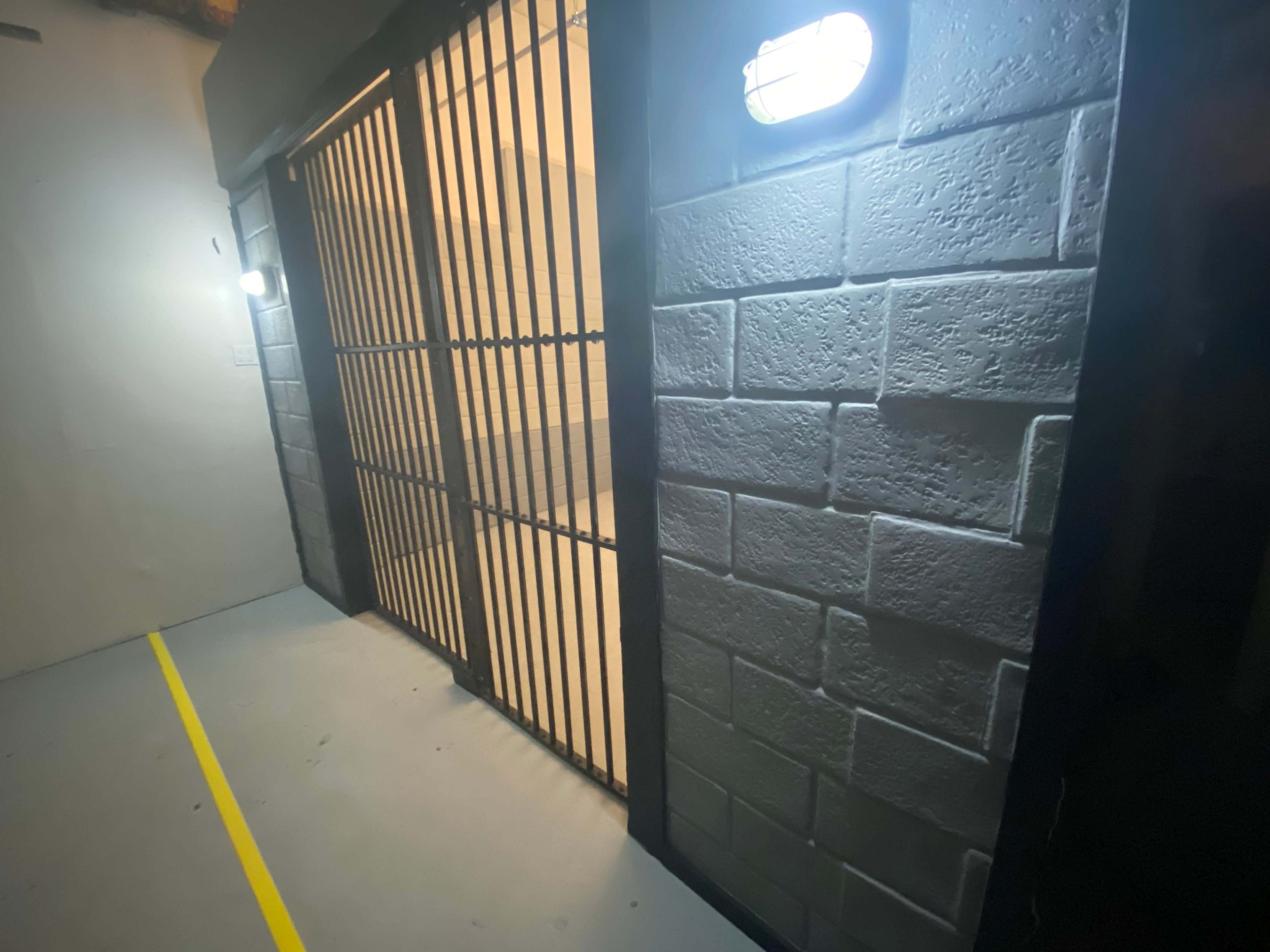 A dimly lit corridor with a barred gate and a textured stone wall.
