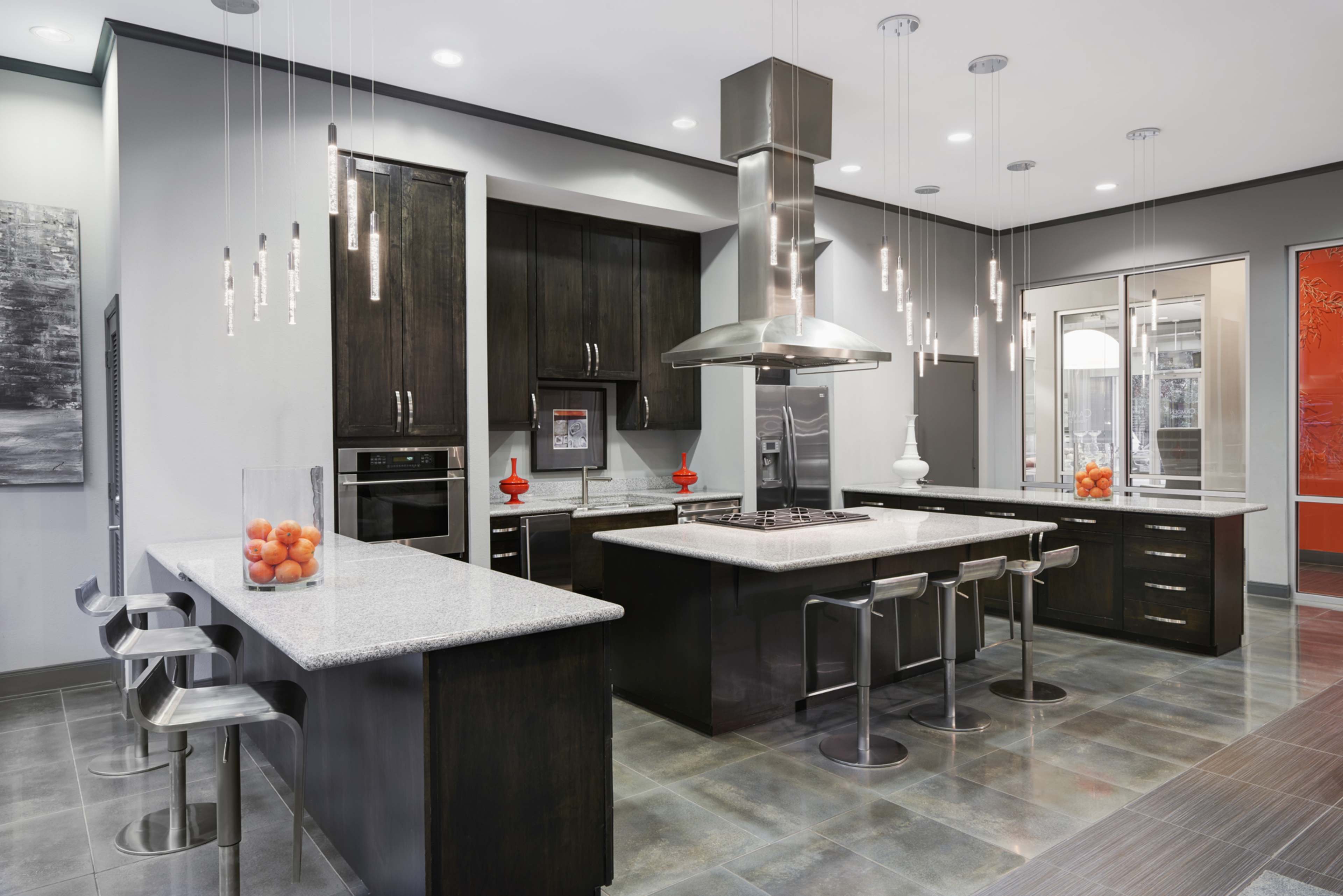 A modern kitchen features dark cabinetry, a central island with a gray countertop, and stainless steel appliances, illuminated by pendant lights.