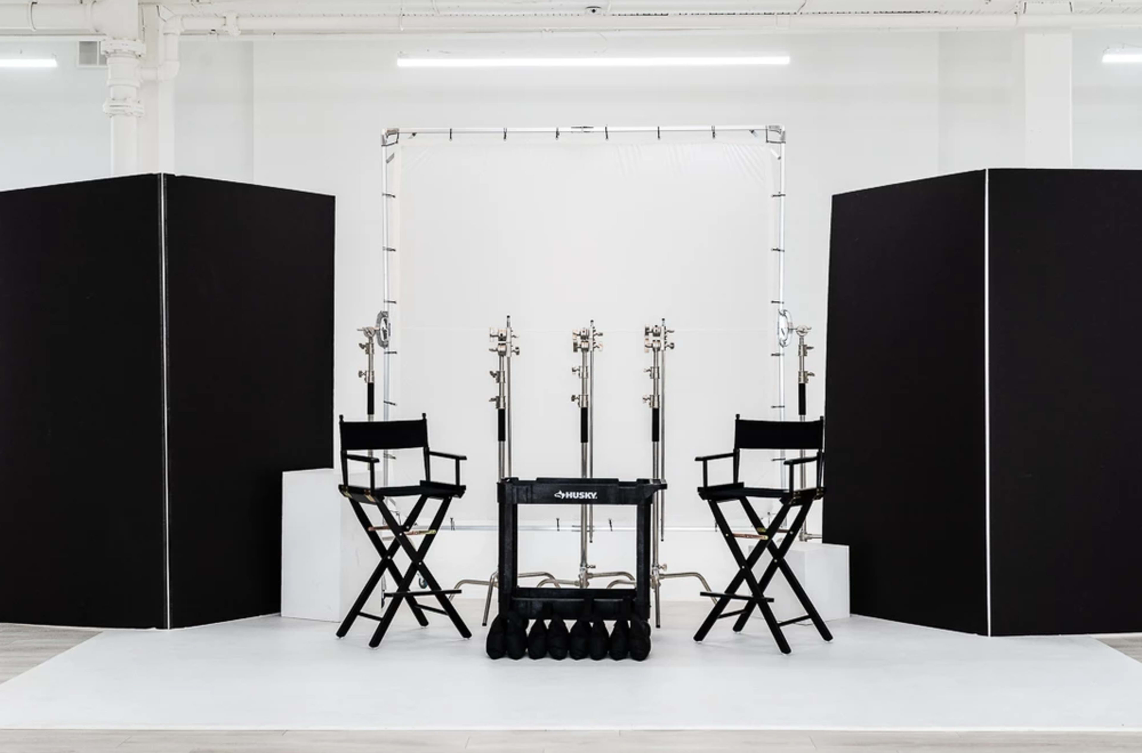 A minimalist photography studio setup with two director's chairs, a backdrop setup, and a portable dolly for lights or equipment.